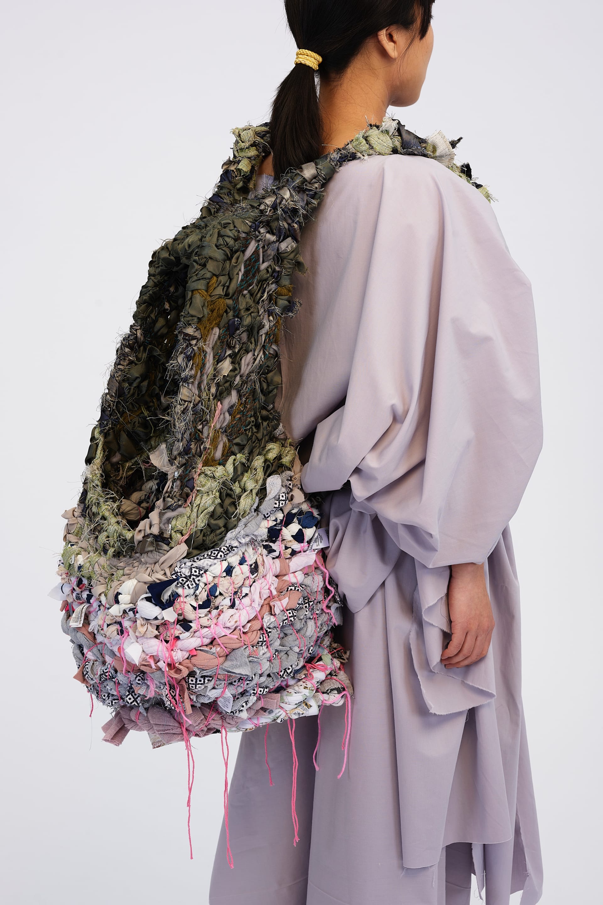 Sculptural backpack of woven upcycled fabric in earth tones, worn with soft, voluminous grey outfit.