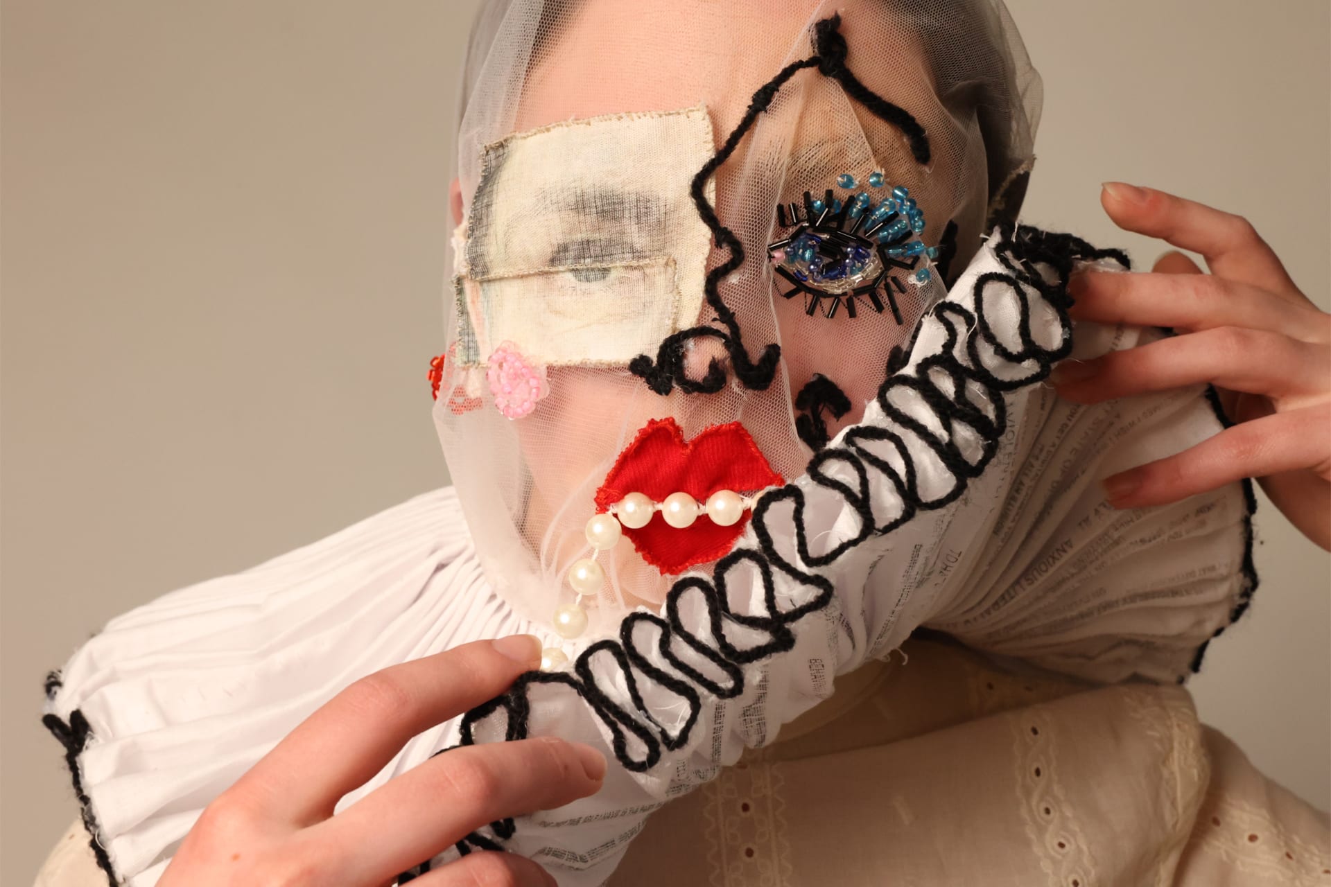 Close up of person wearing a mesh mask with fabric ruff. The ruff is being lifted and is concealing some of the face.