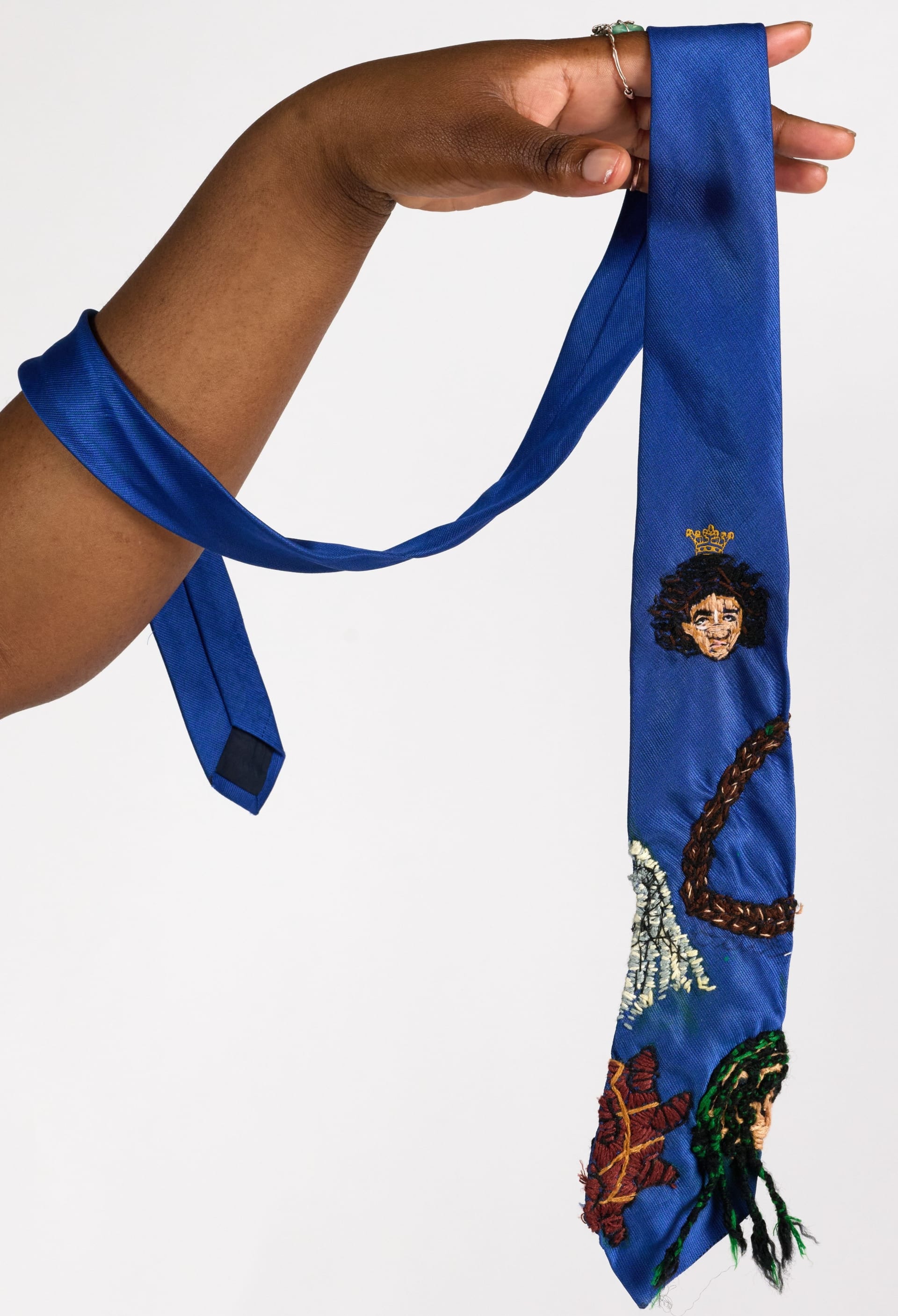 An electric blue tie embroidered with different hairstyles, Bantu Knots ,cornrows. locs, braids and a poirtrait of Zulaikha Patel
