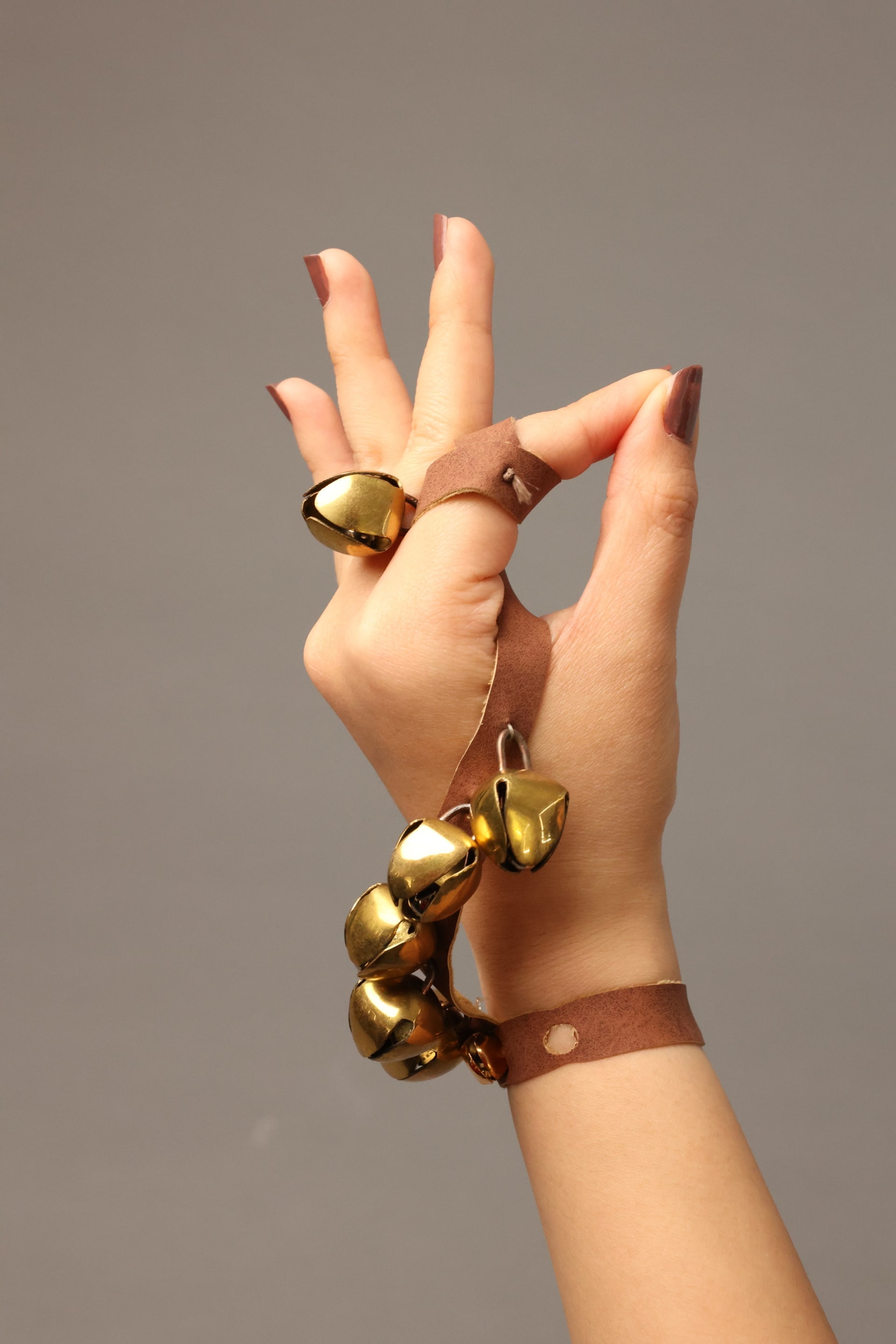 An image of a hand in a graceful pose wearing Khanak—hand jewellery with golden bells on leather straps, inspired by traditional Indian ghungroos.