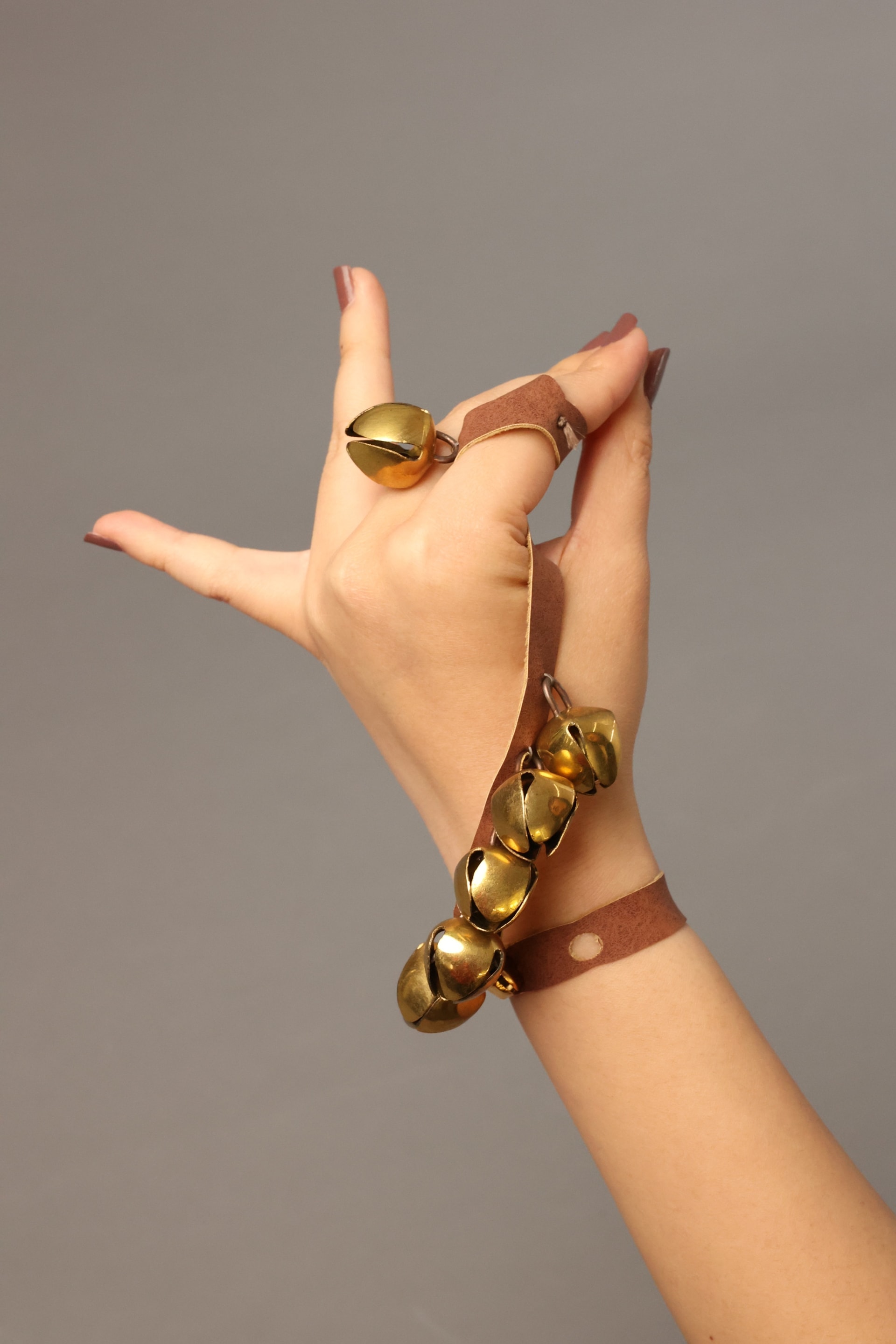 An image of a hand in a graceful pose wearing Khanak—hand jewellery with golden bells on leather straps, inspired by traditional Indian ghungroos.