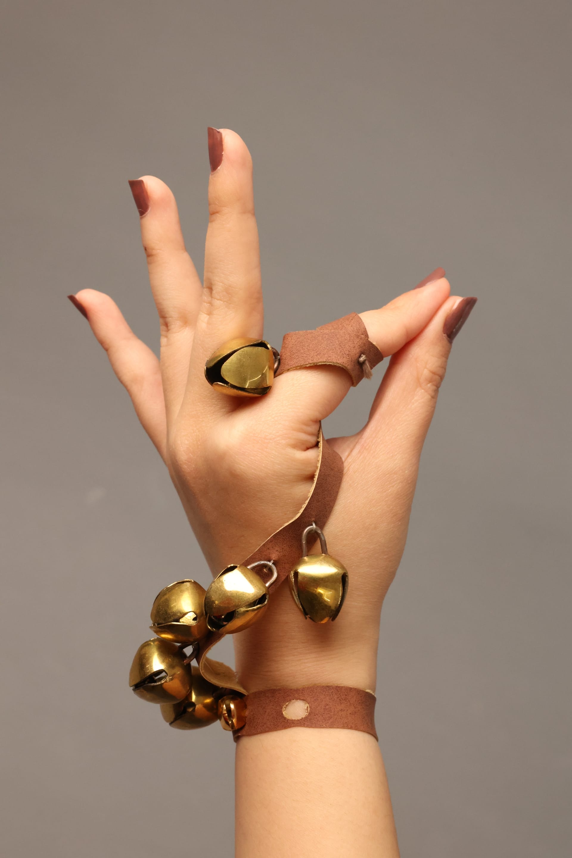 An image of a hand in a graceful pose wearing Khanak—hand jewellery with golden bells on leather straps, inspired by traditional Indian ghungroos.