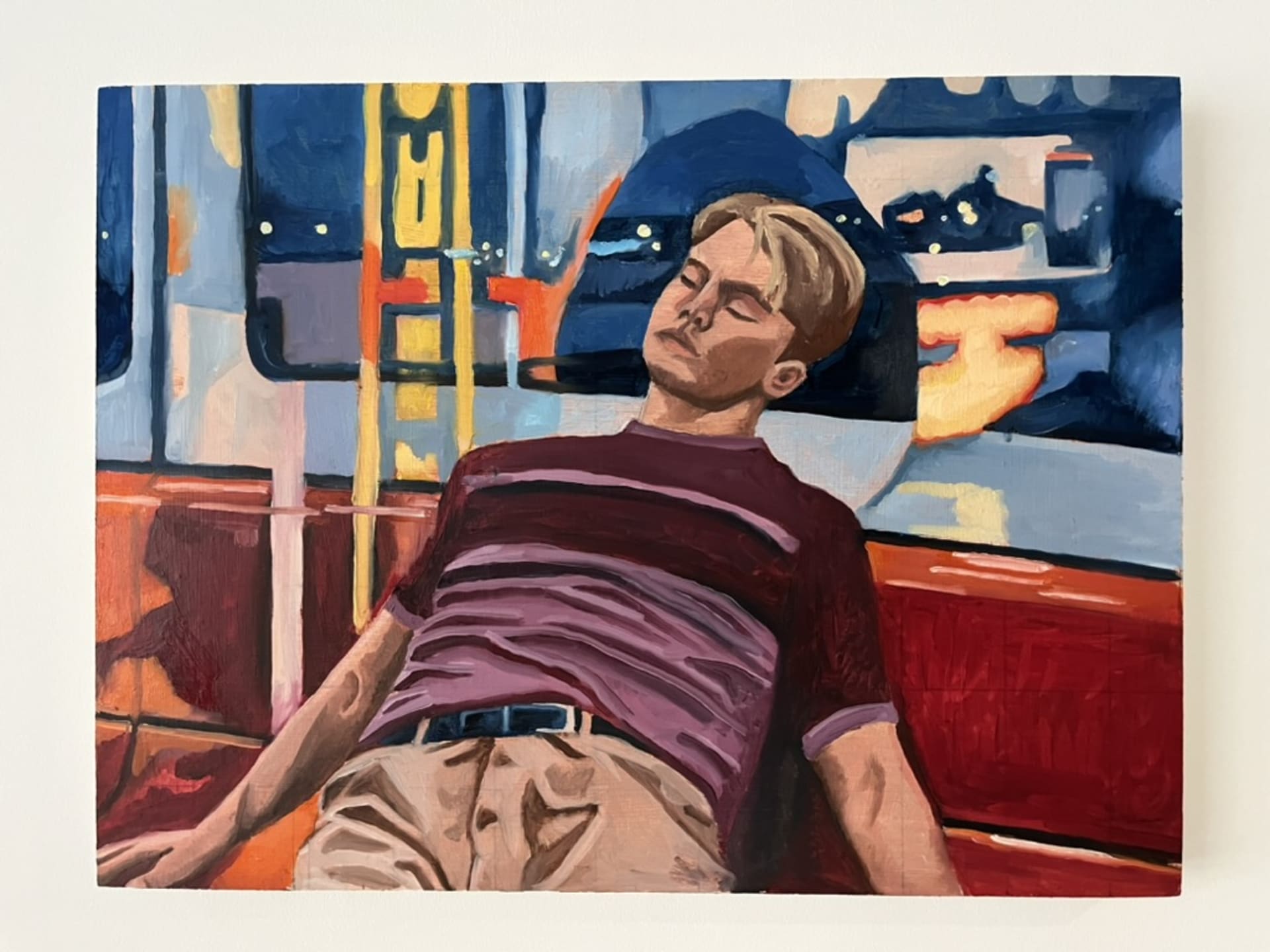 A painting of a young man sleeping on a red subway seat at night, with blurred city lights visible through the window behind him.