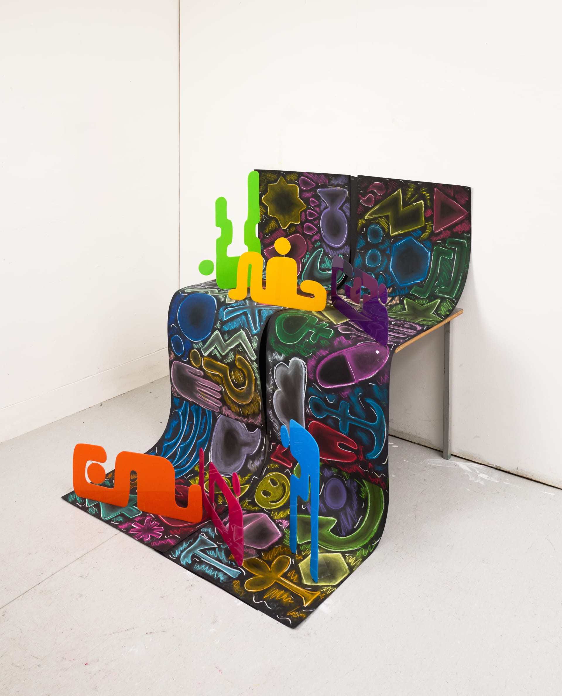 An installation using acrylic plastic figures that stand freely in front of a backdrop of vibrant symbols and shapes.