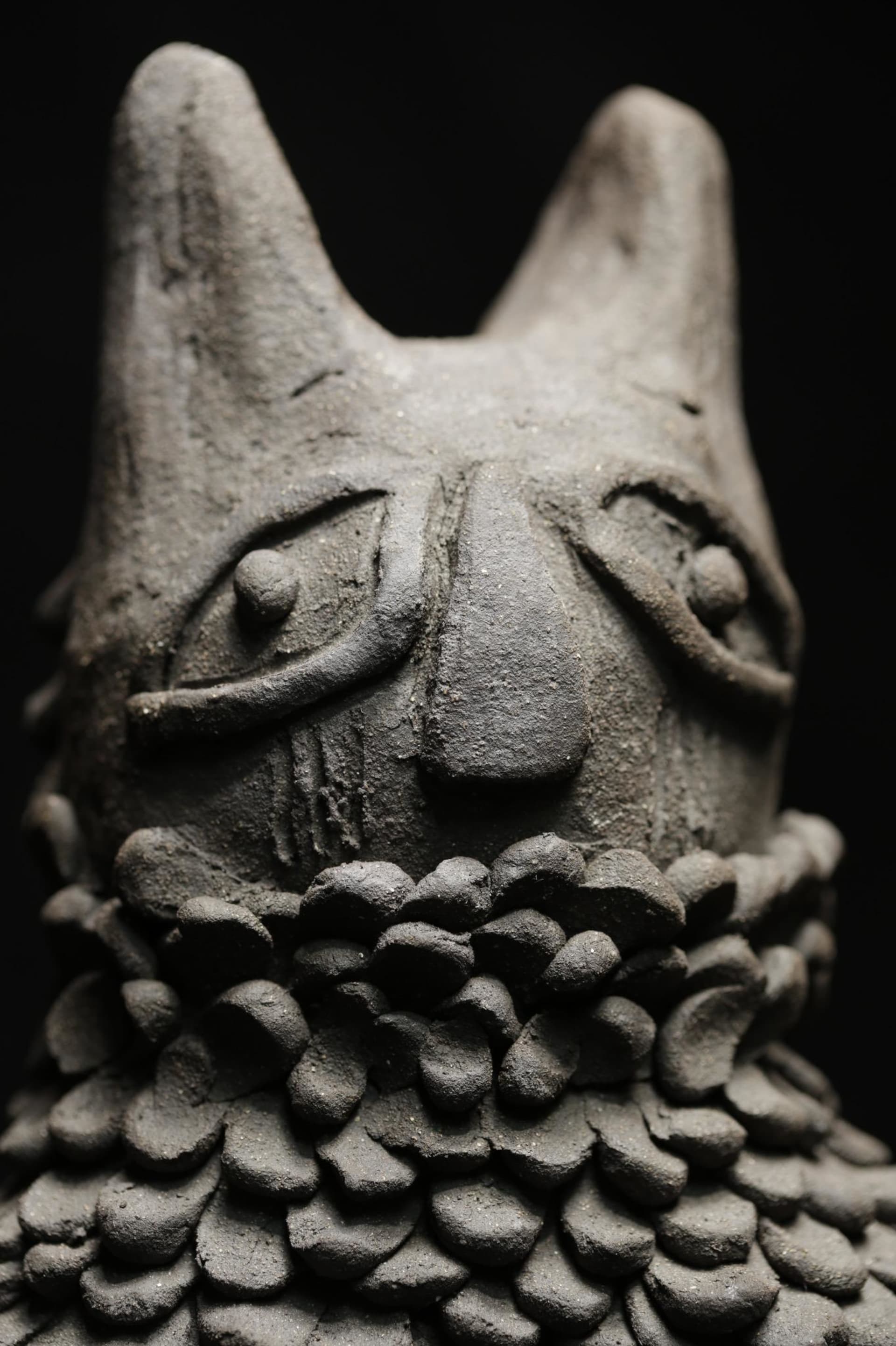 The figure features exaggerated eyes, a prominent nose, and layered, scale-like textures around its base, meant to symbolise the attire worn.