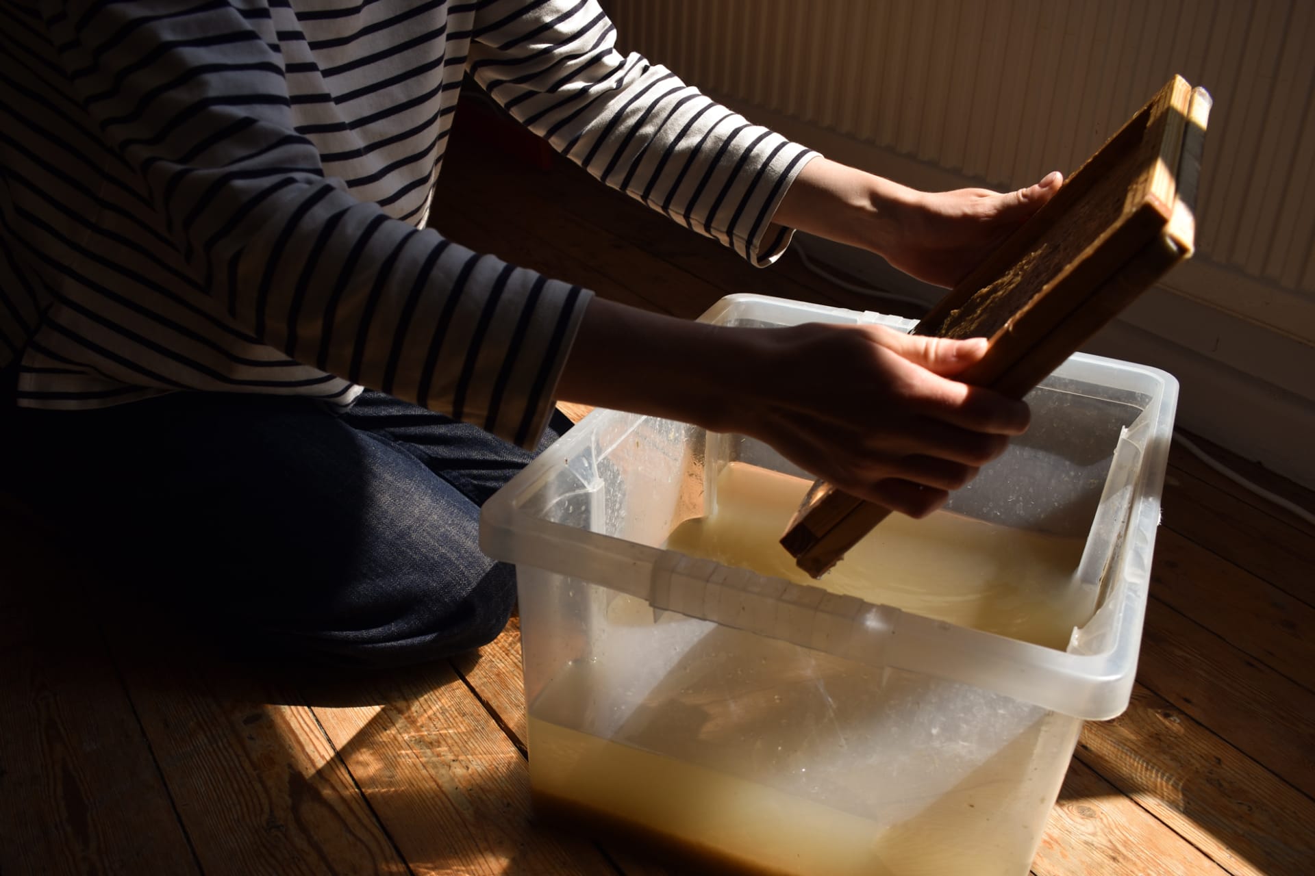 Pulling a sheet of paper from a plastic box with a mould and deckle