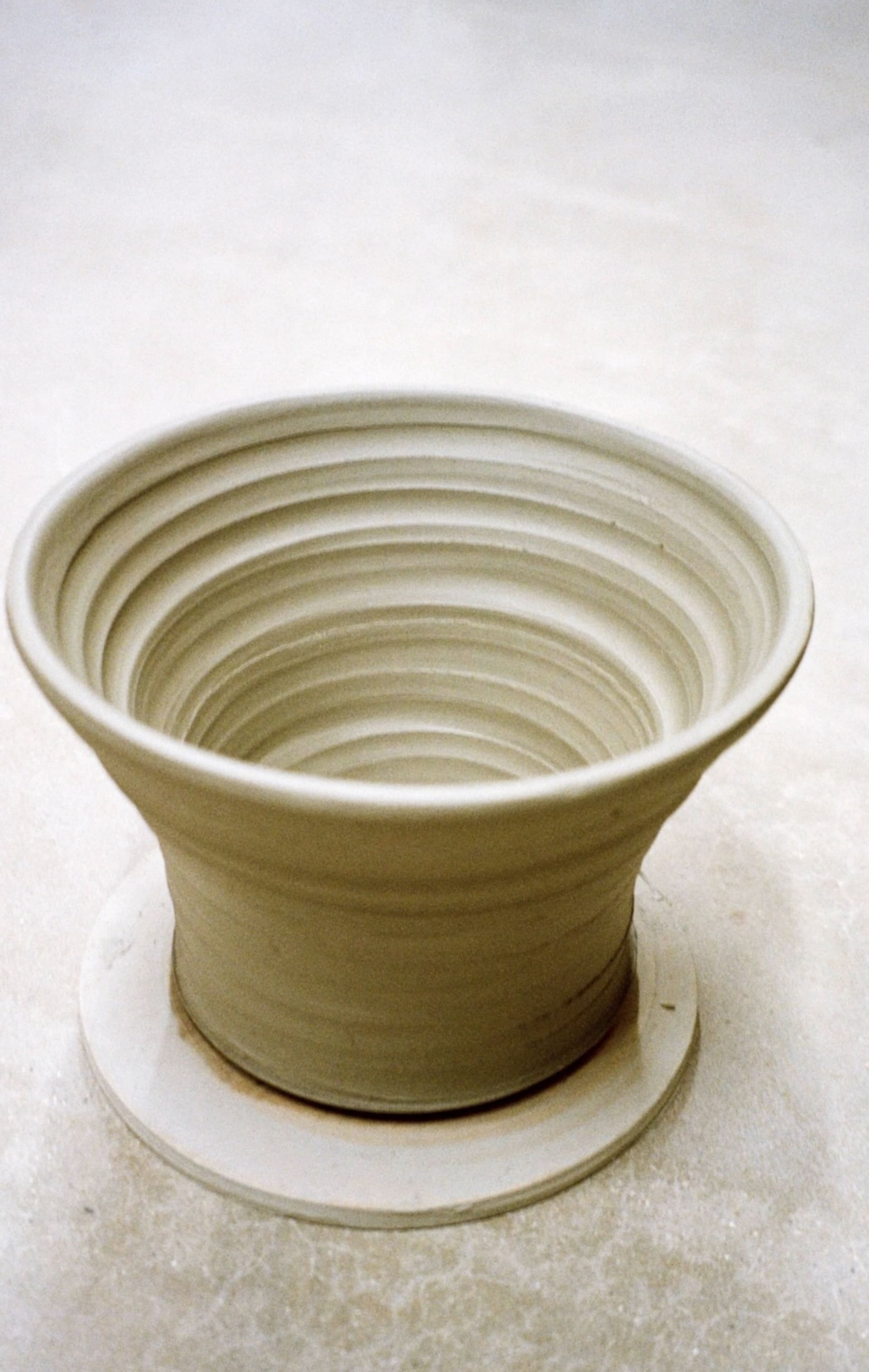 a flared stoneware pot on a grey concrete floor that have just been removed from the wheel
