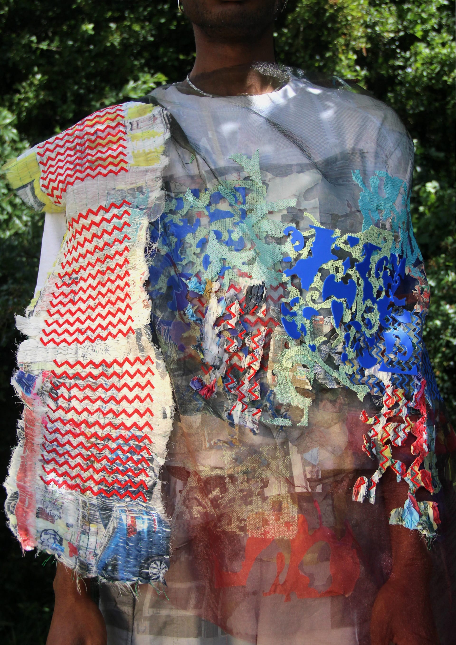 the model is stood facing the camera, under a tree. the focus is on the fabric the model is wearing which has been embellishing and printed on.