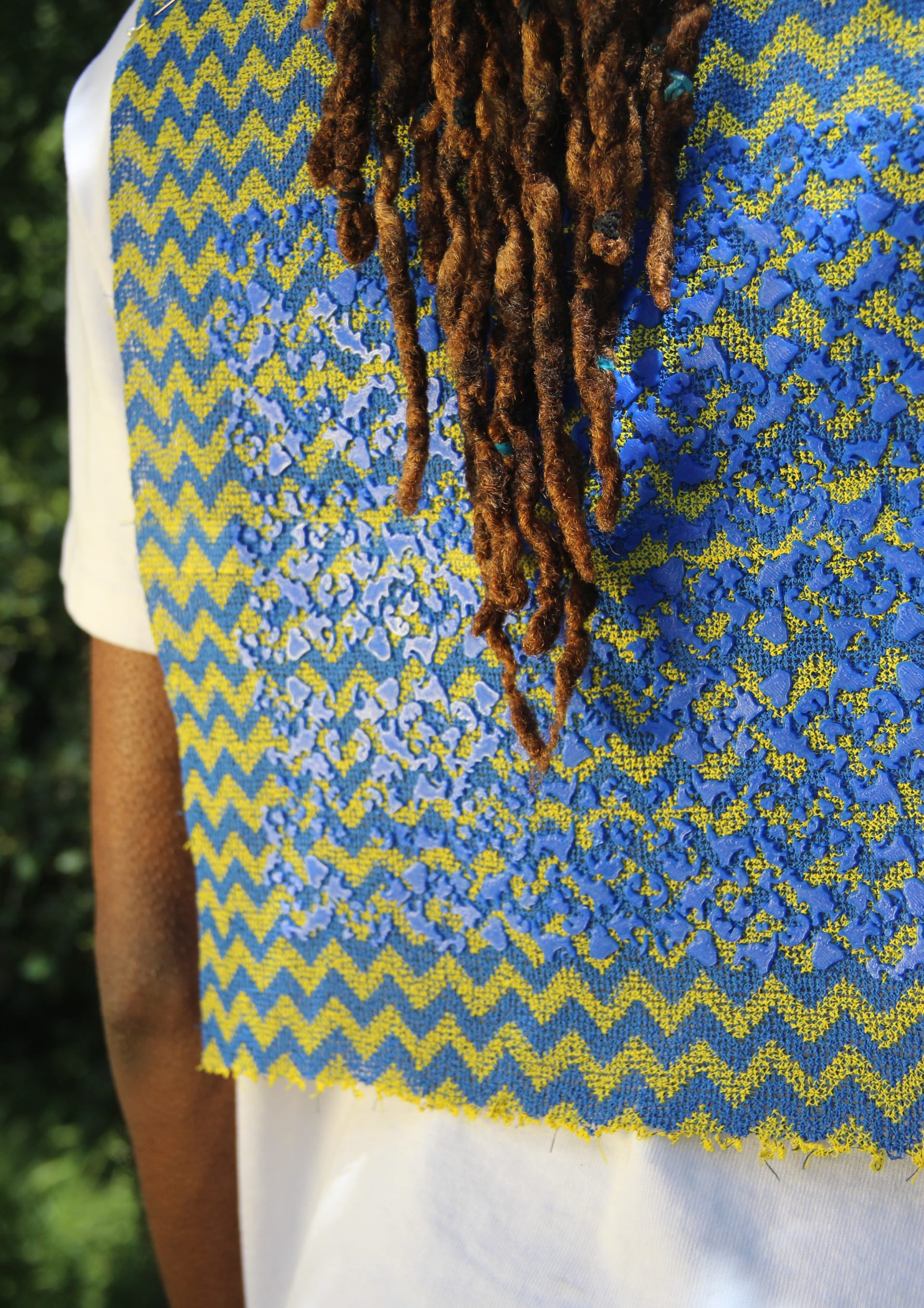 the photo shows a close up of a yellow and blue striped fabric on the back of someones shirt. you can see another blue pattern on the fabric