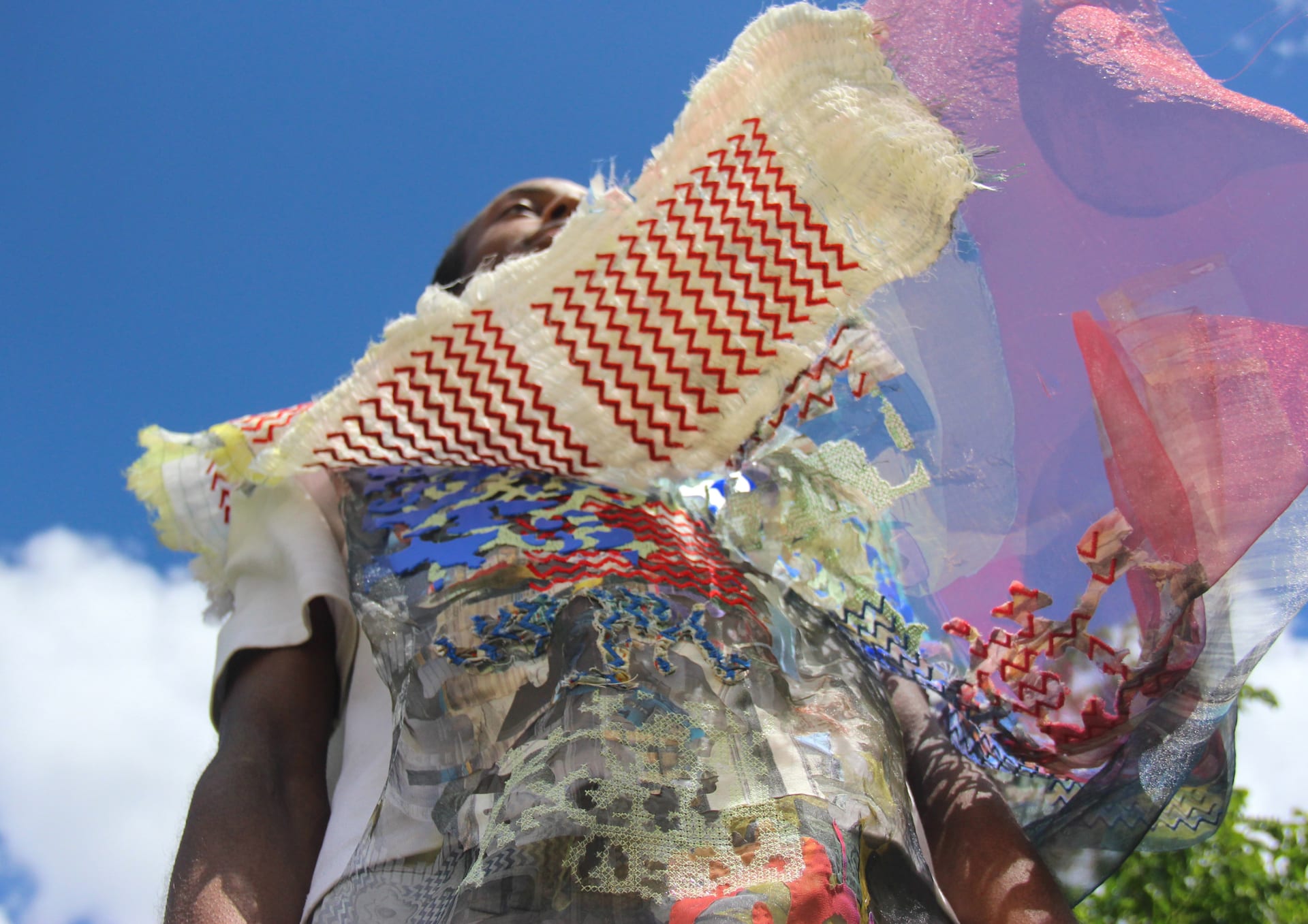 stood beneath the model, the fabric he is wearing blows in the wind, revealing colourd and patterns beneath that twin well with the blue skies