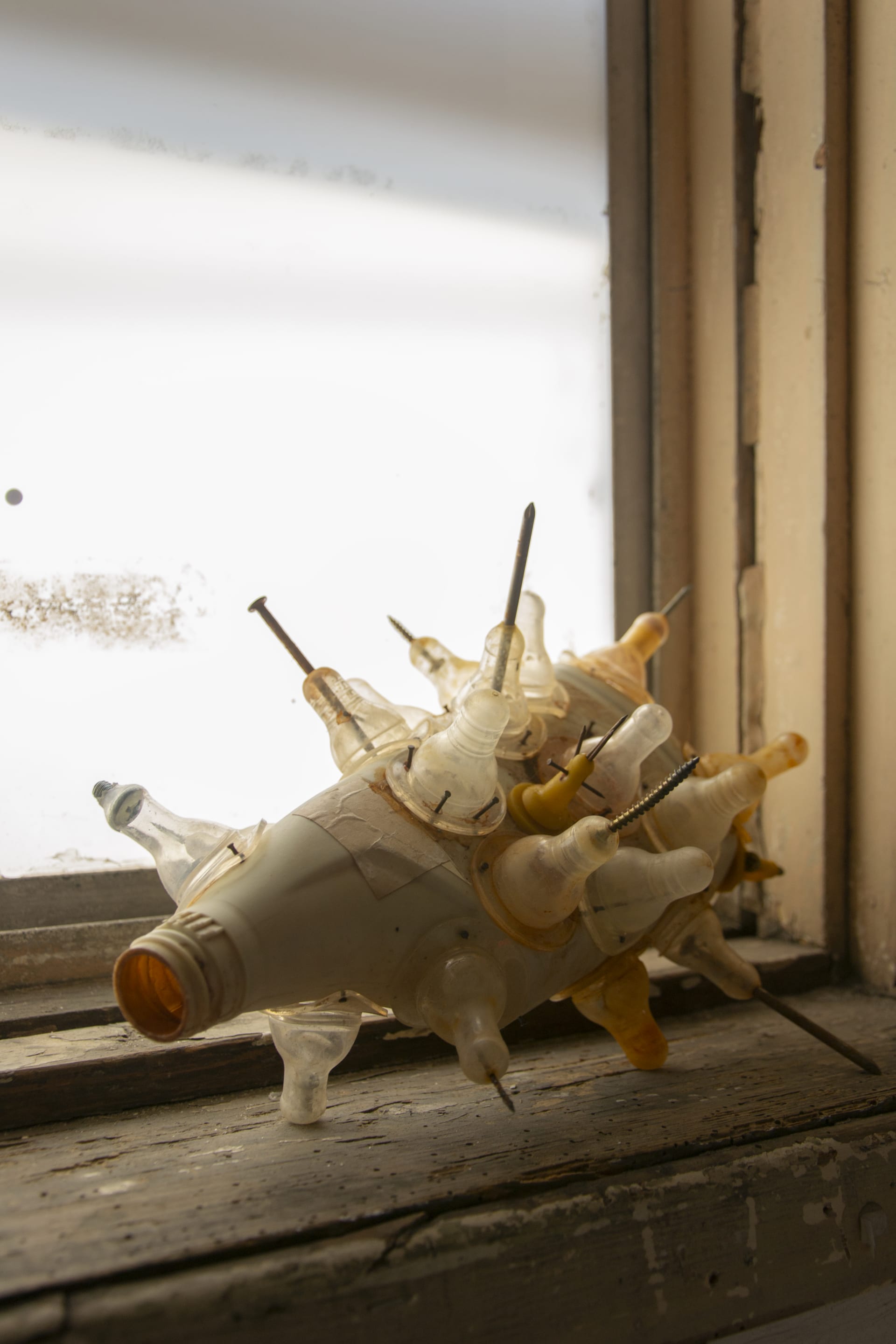 A discarded bottle with bottle nipples nailed onto the outside with rusted nails and screws protruding through the tip of the nipples.