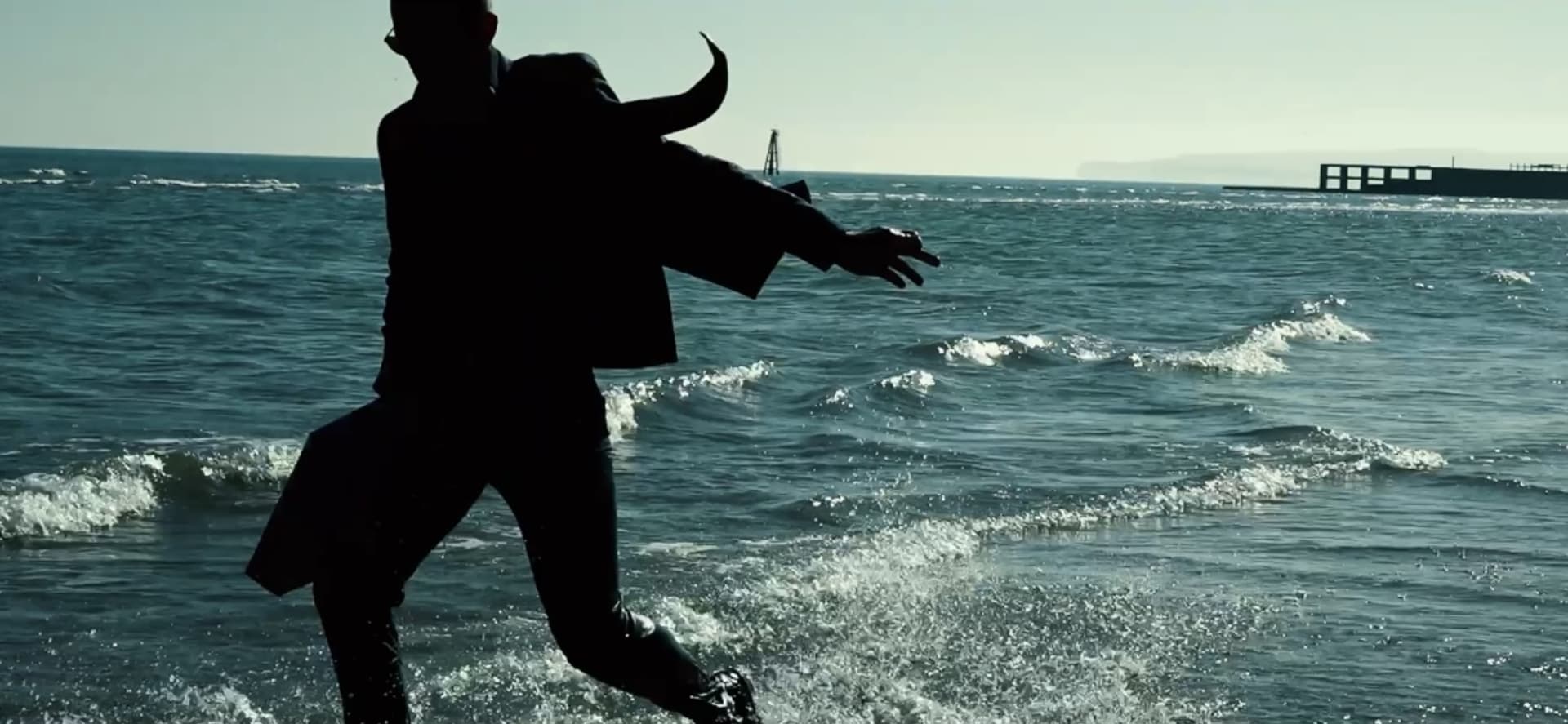 Silhouette of a suited man splashing through the ocean sore.