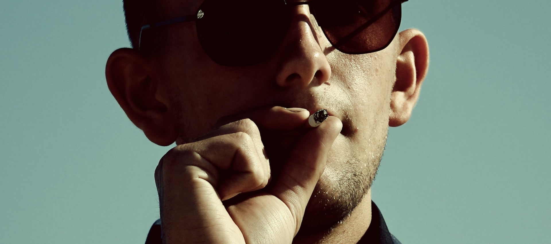 Close up of man smoking cigarette, with sunglasses on.