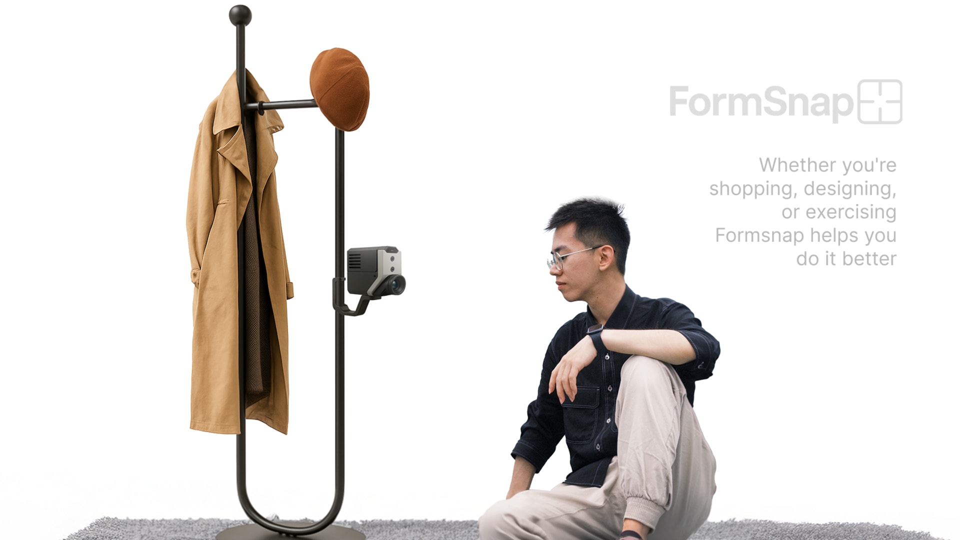 A man sitting on the ground next to cloth rack which has a coat hanging on it and a digital device plugged to it.
