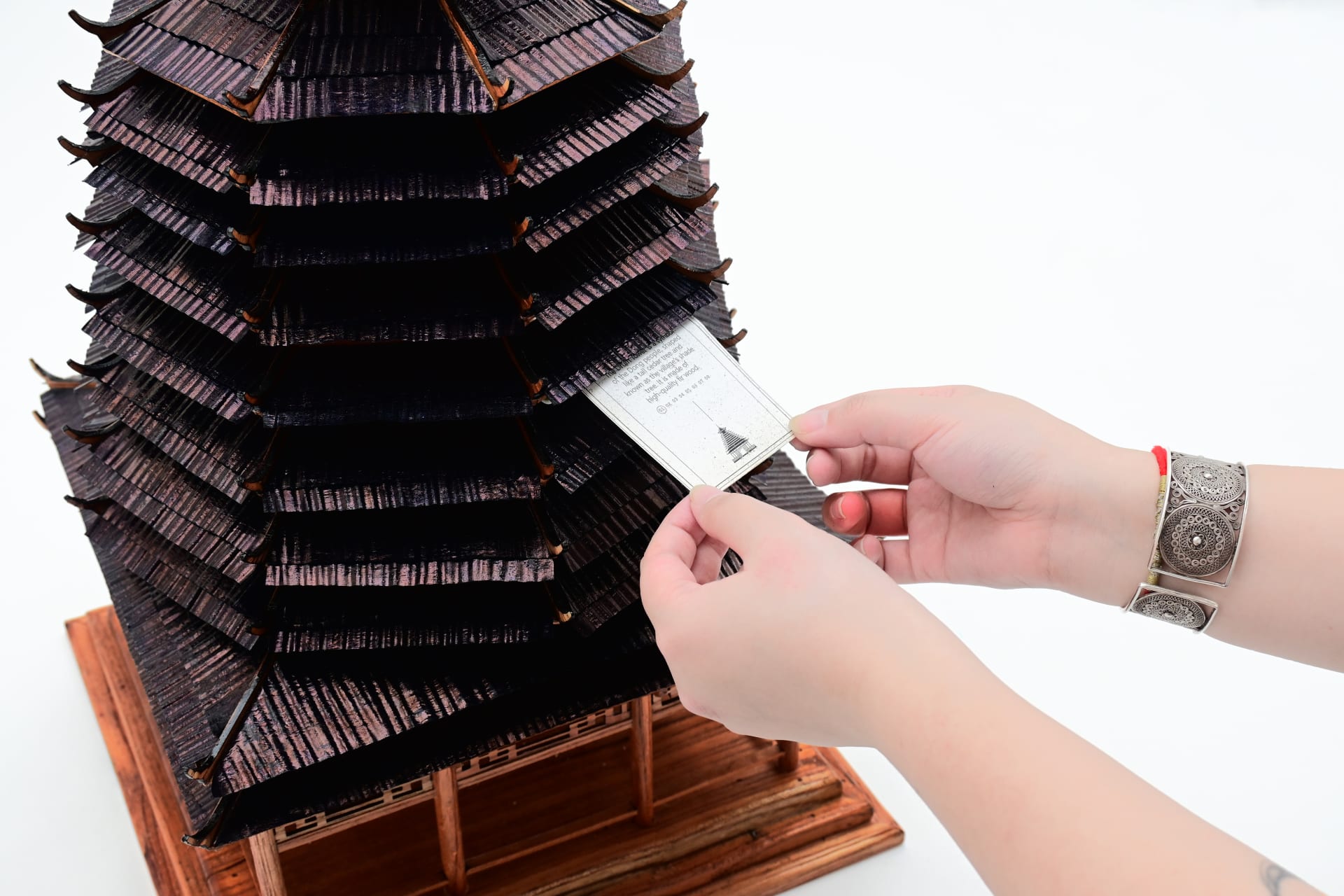 A close-up of a person pulling out a scroll from beneath the roof of the drum tower model.