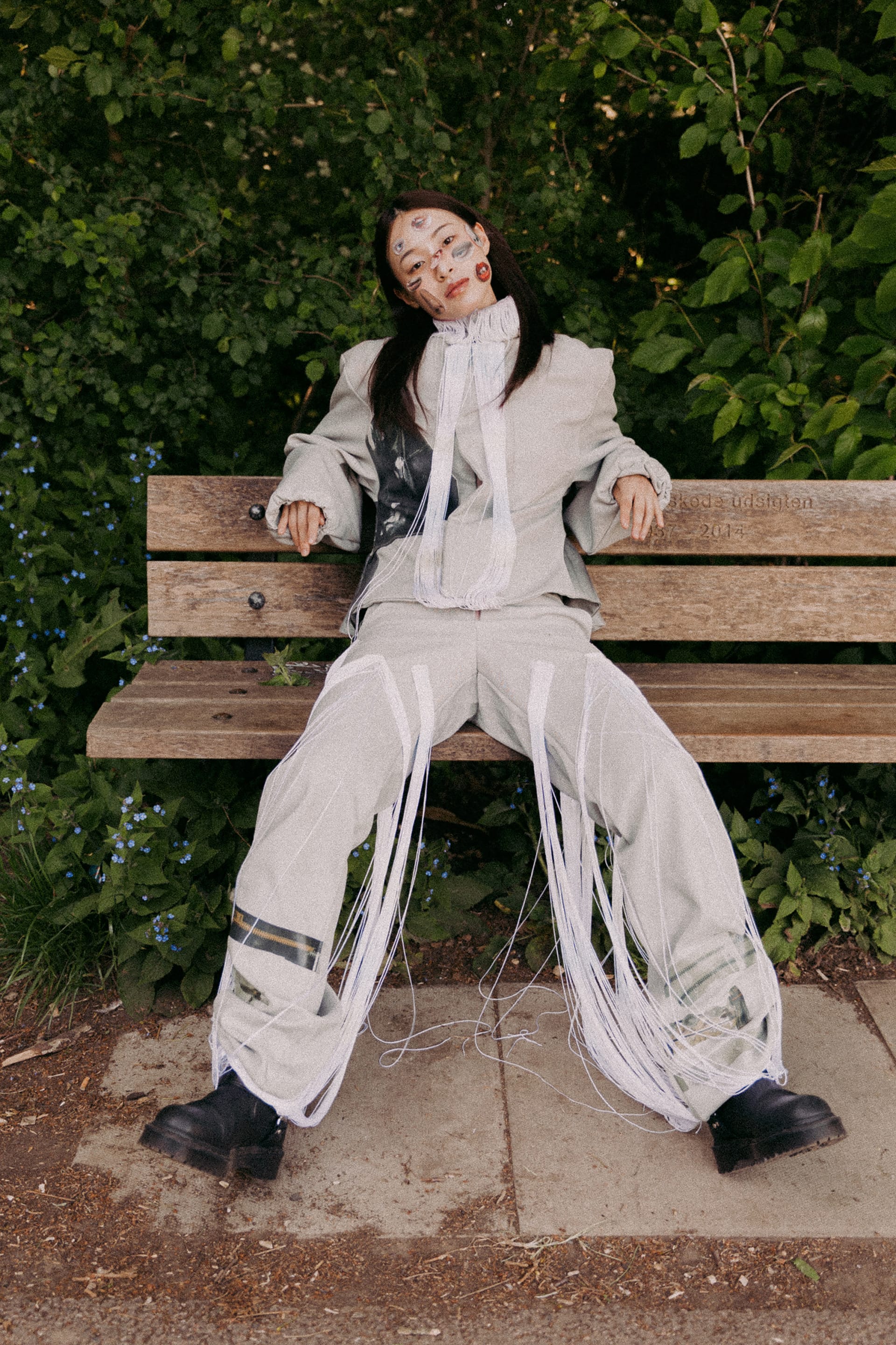 A girl wearing collage makeup poses on a bench.