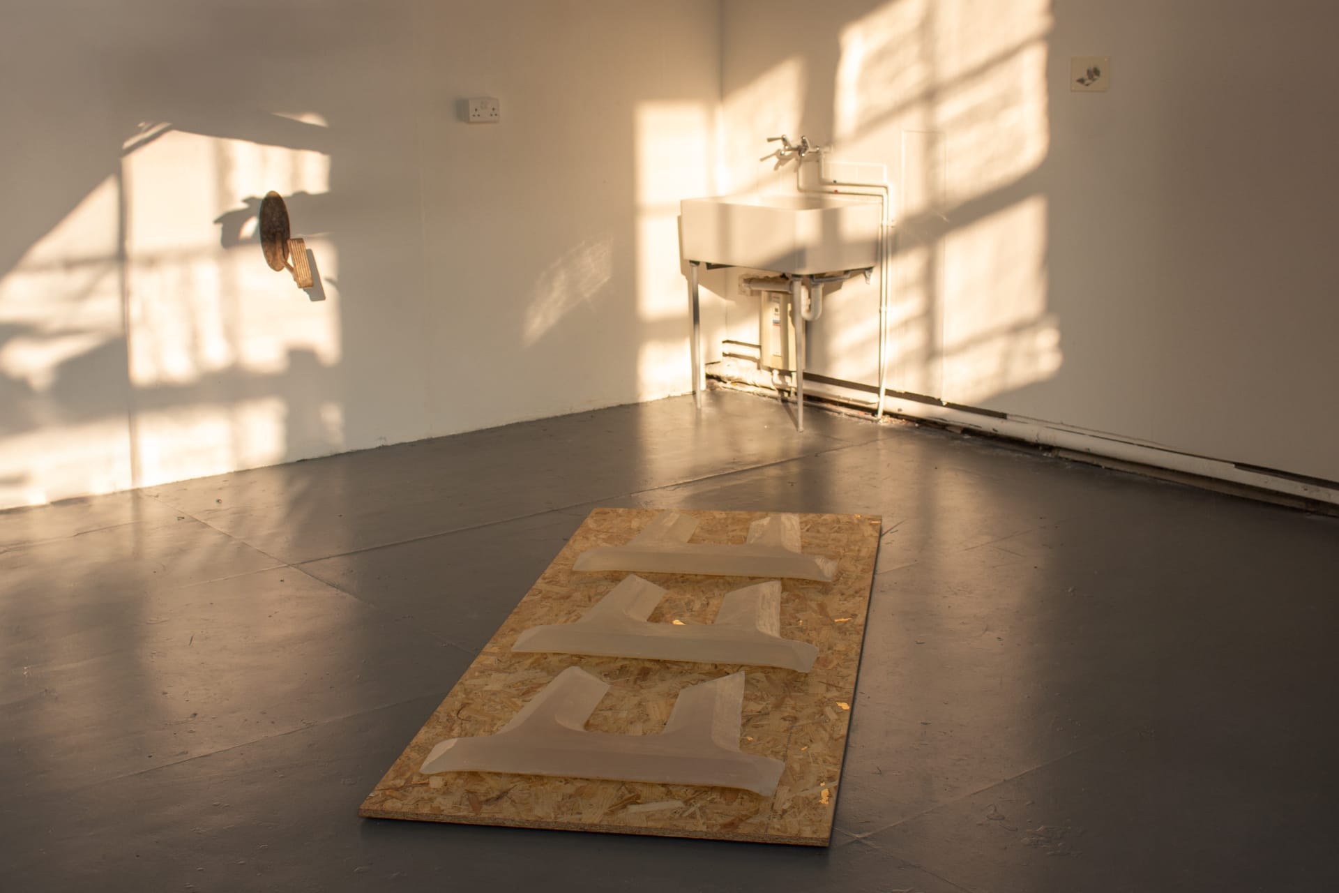 wide installation picture of a sheet of OSB with 3 soap anchors placed atop, a bronze car pedal on the wall to the left, and an a5 print to the right