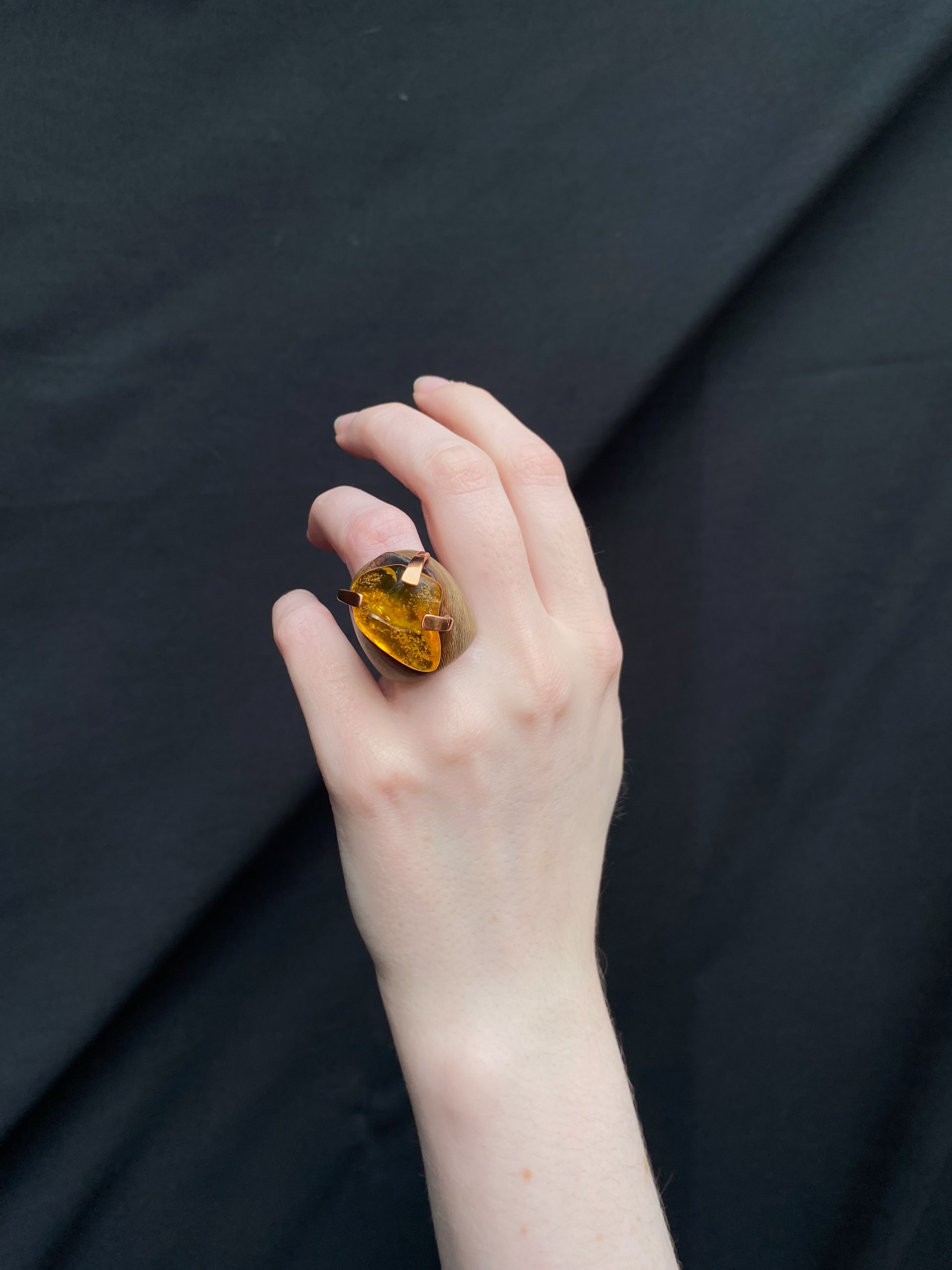 A ring with a large yellow amber set on top of the wood by 3 copper claws 