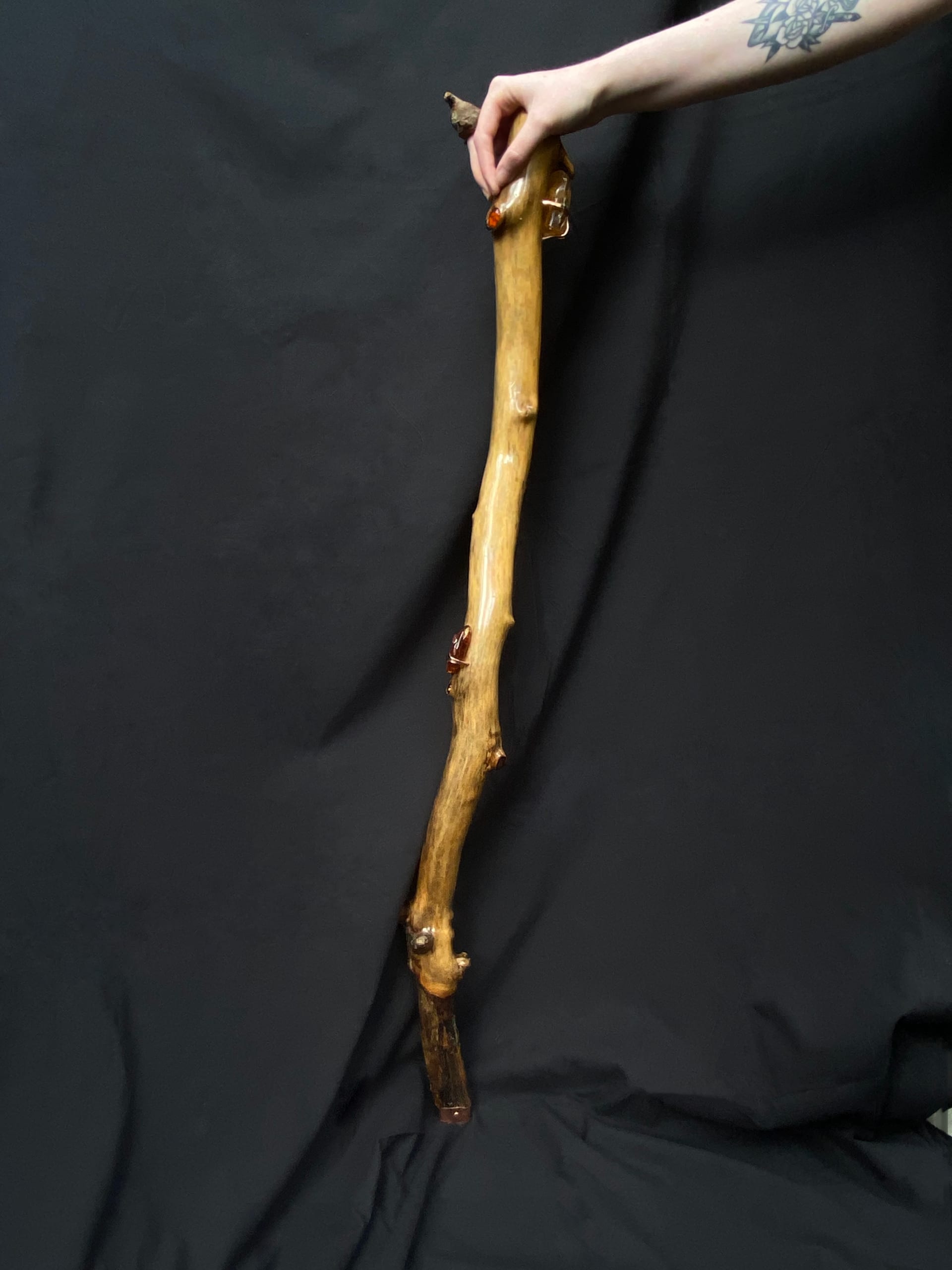 A walking stick made from a branch with a bend towards the bottom. It has three large ambers set with copper, four small cabochon ambers in the wood