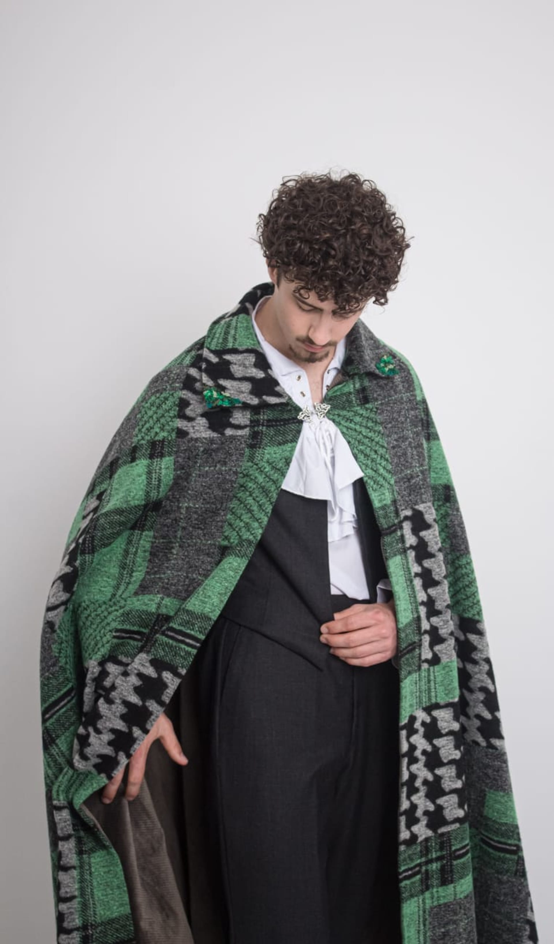 Green cape with grey waistcoat and trousers and a ruffle collar shirt.