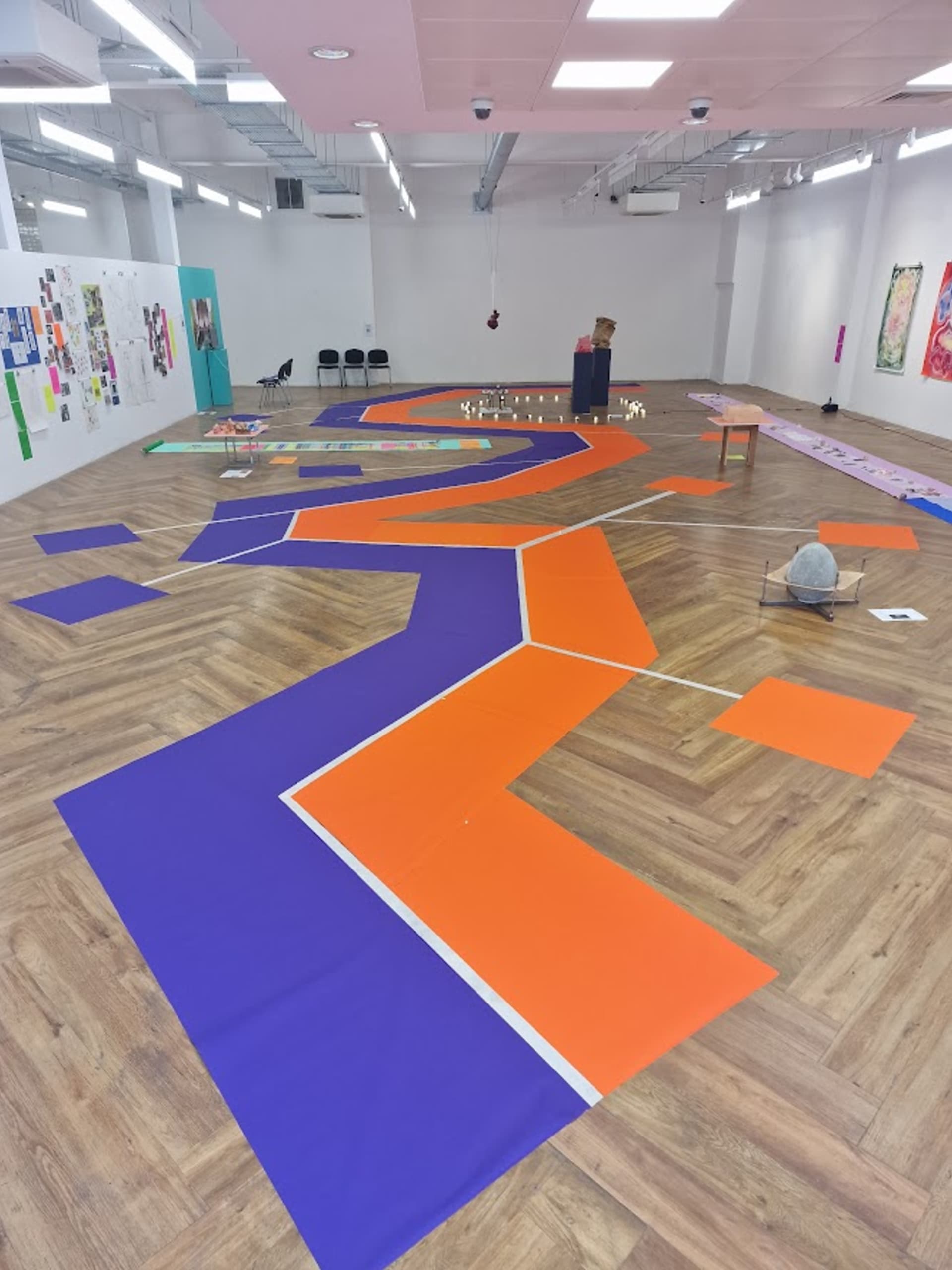 A long view down a modern gallery, with broad irrregular stripes of orange and purple demarcating the course for placing dominoes