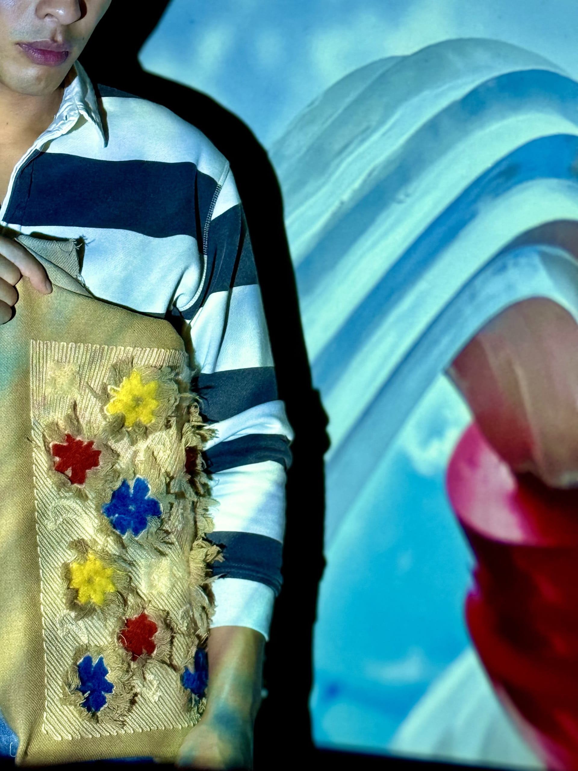 Shredded fringing around red, yellow, and blue flower pattern. Across chain-stitched mimicking woven fabric.