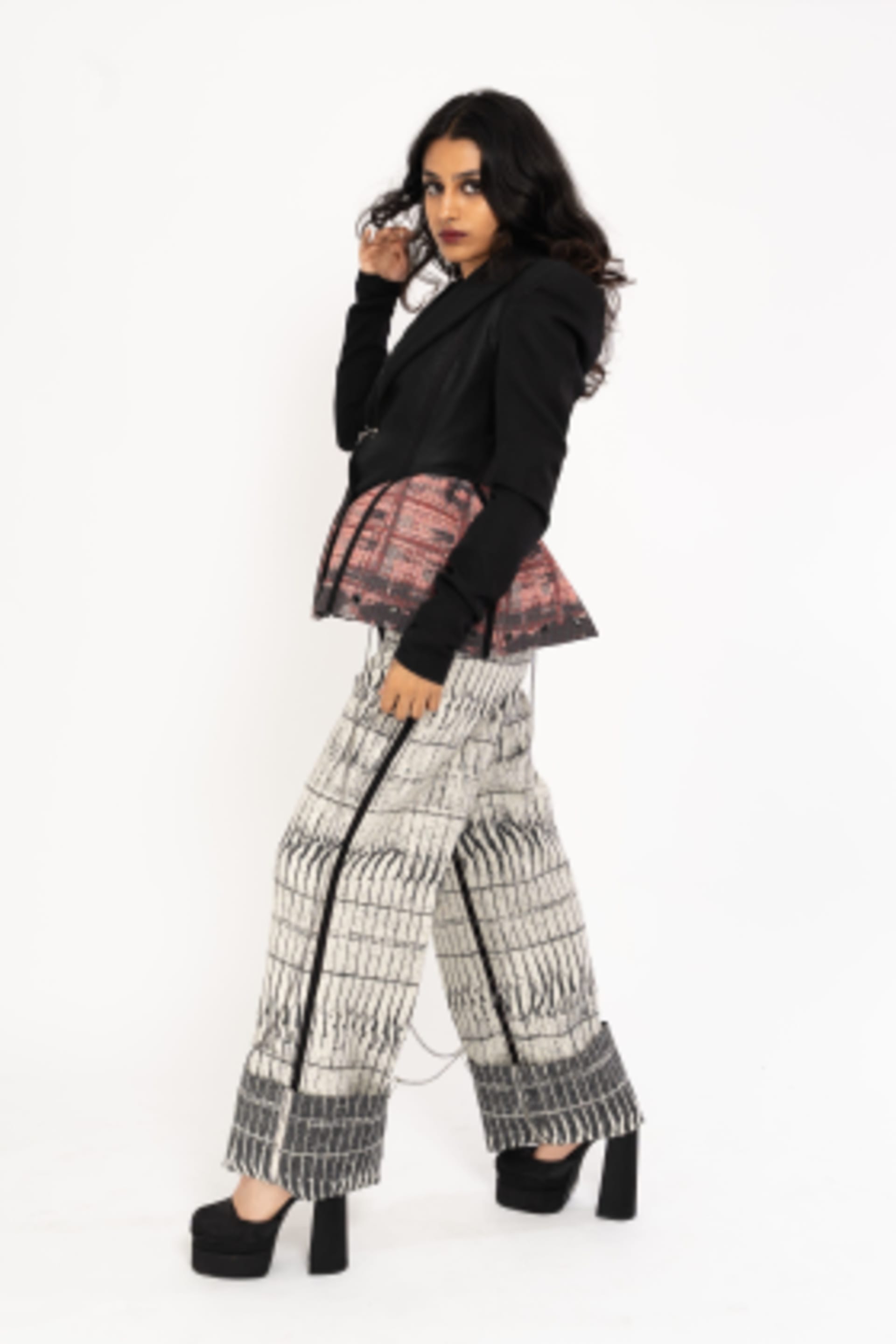 Female model wearing a jacket and wide leg, turned-up trousers. Self designed Hainsworth fabric, featuring graphic black, white and red design.