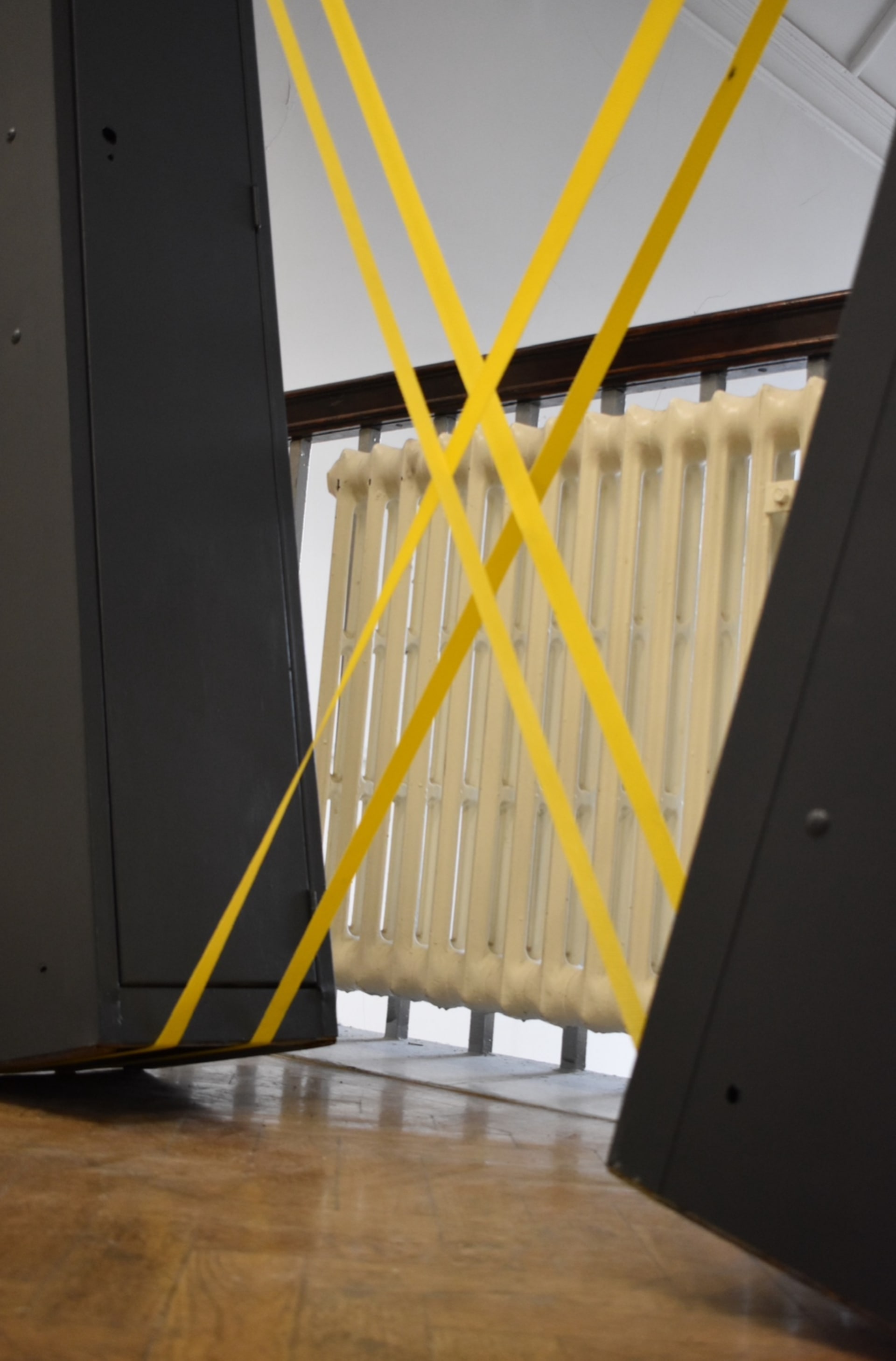 Close up of two painted grey metal lockers, tilted and balanced, supported by two yellow cam buckle straps that cross over the lockers.