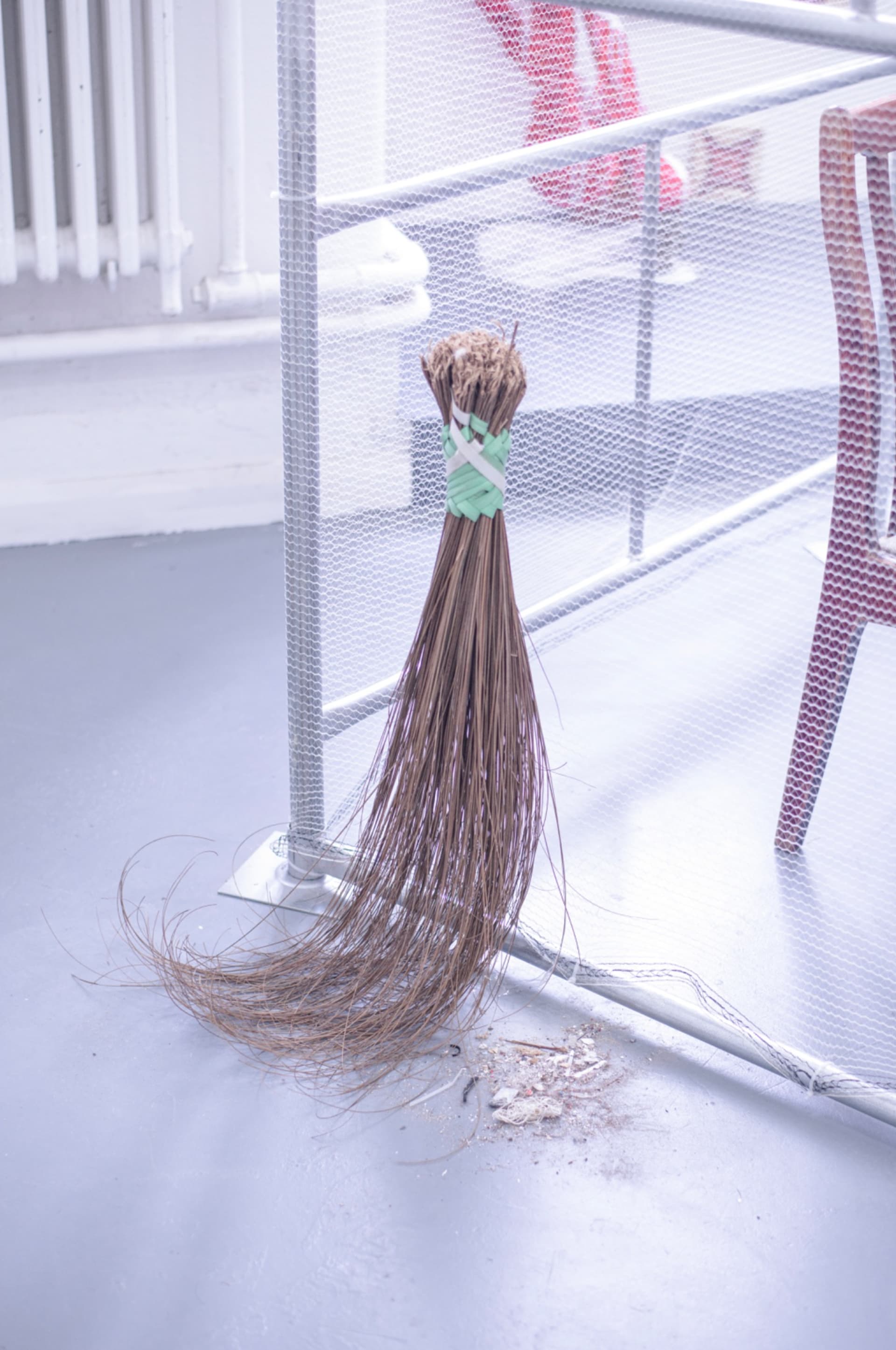 Scaffolding tower with debris netting encloses a stool atop a chair and suspended carpet roll, accompanied by a broom and pile of site-collected dirt.