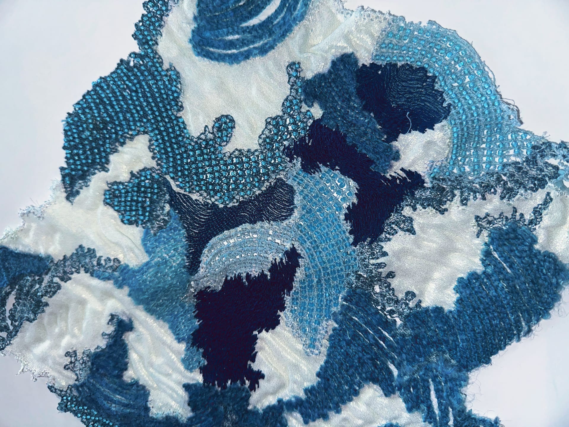 The combination of different materials and techniques. Shiny fabric patchwork embroidery weaving and lace connected with beads.