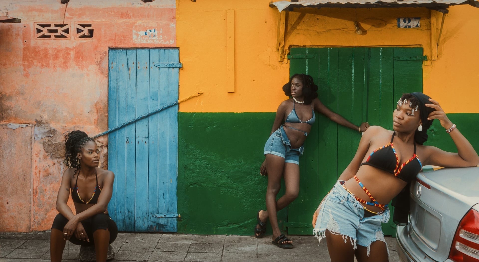 Three women modelling swimwear in denim shorts. They are standing in front of colourful doors and walla