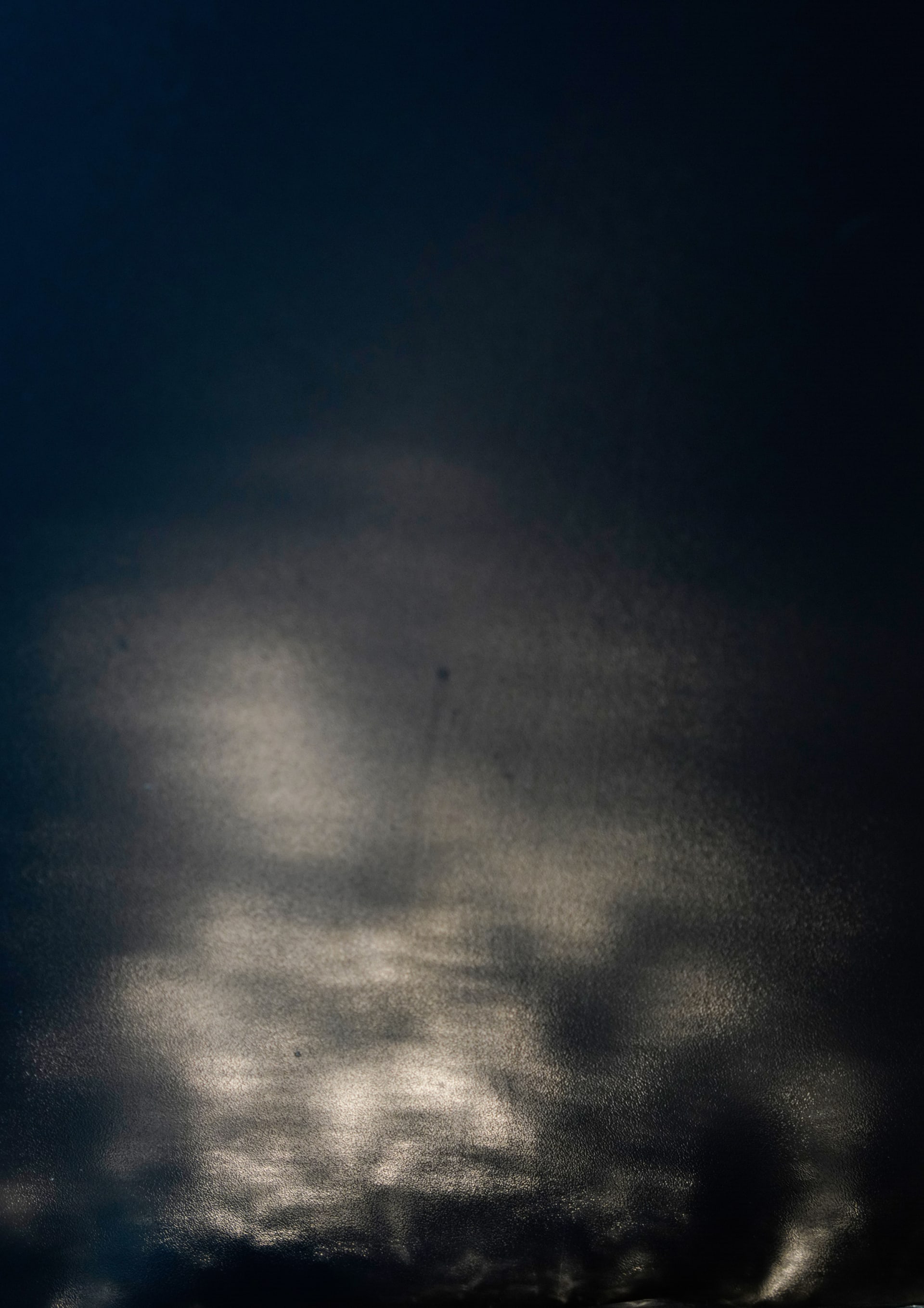 The image shows soft, diffused light across a dark surface, resembling reflections or mist.