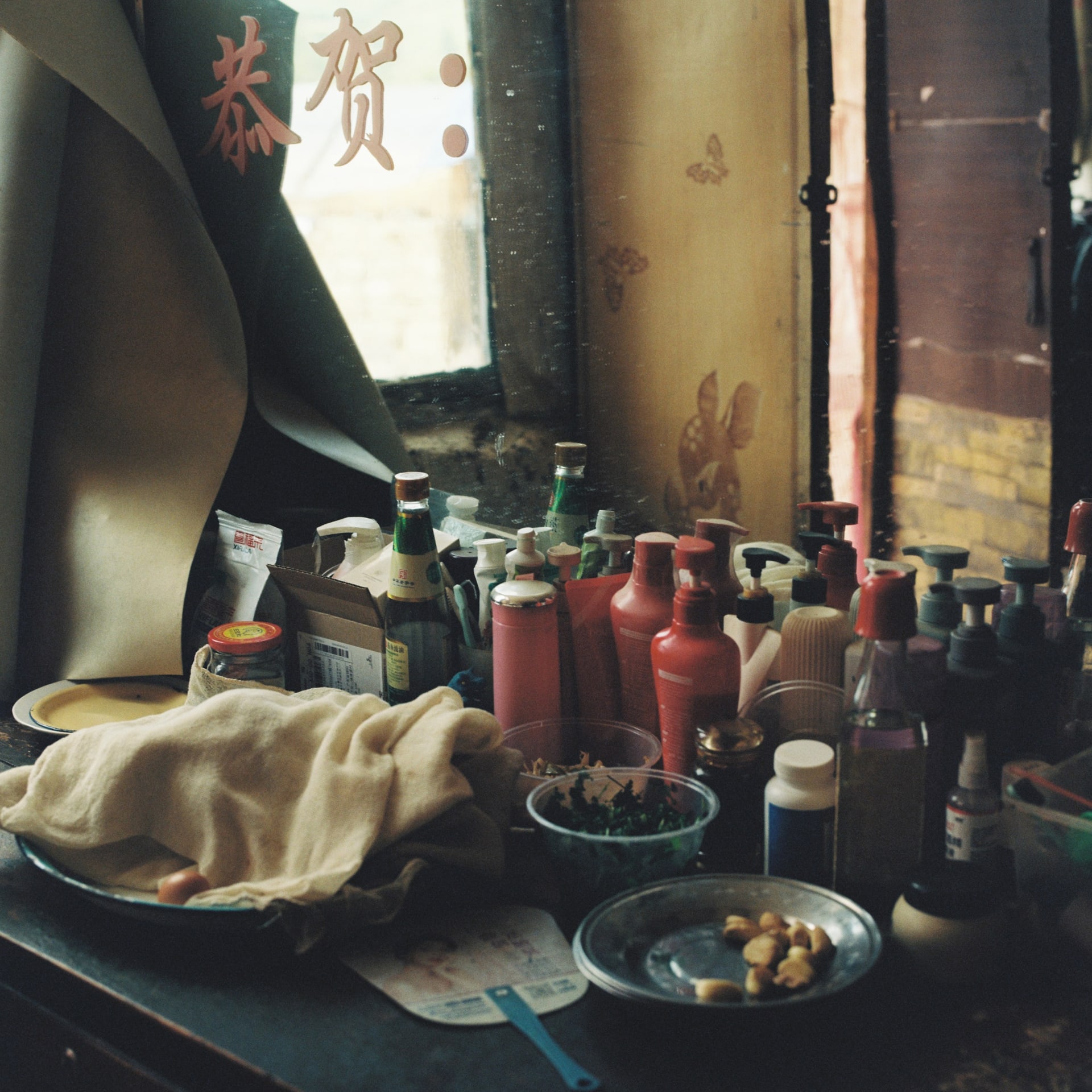 A cluttered table with bottles, cloth, and food in front of an old mirror.