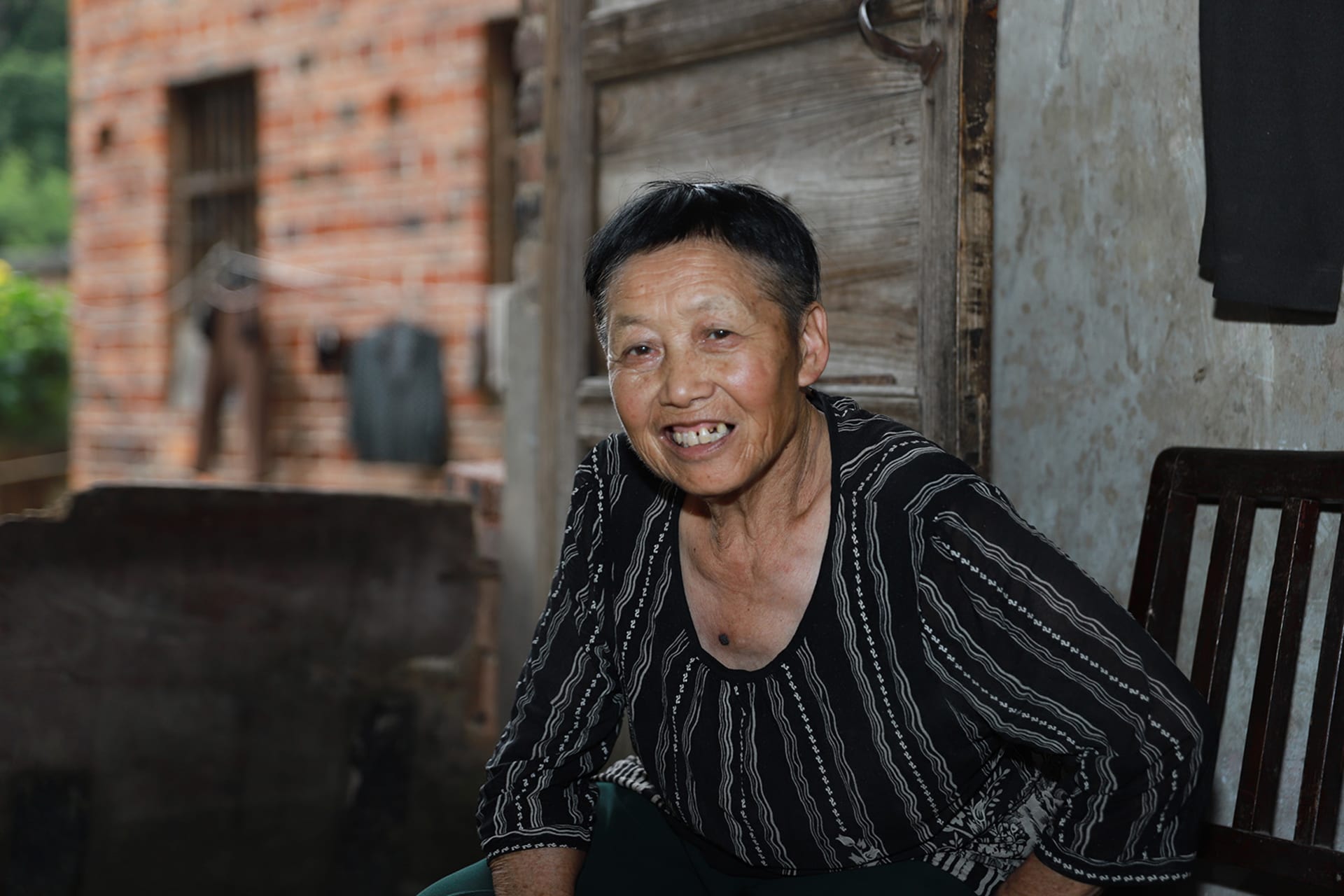 An elderly woman sits in a chair, smiling.