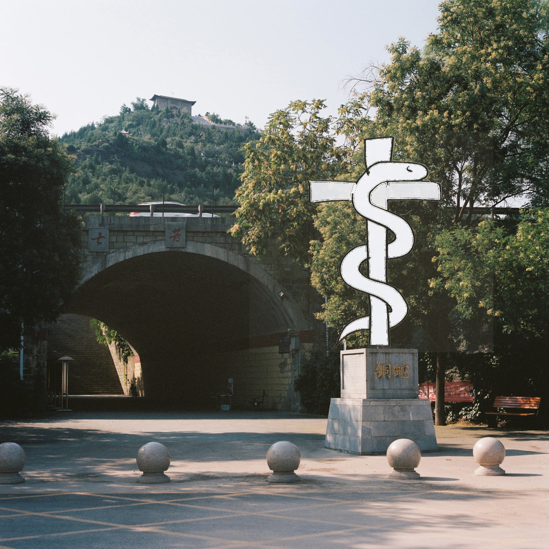 A hand-drawn snake and cross sculpture stands in front of a tunnel entrance surrounded by trees.
