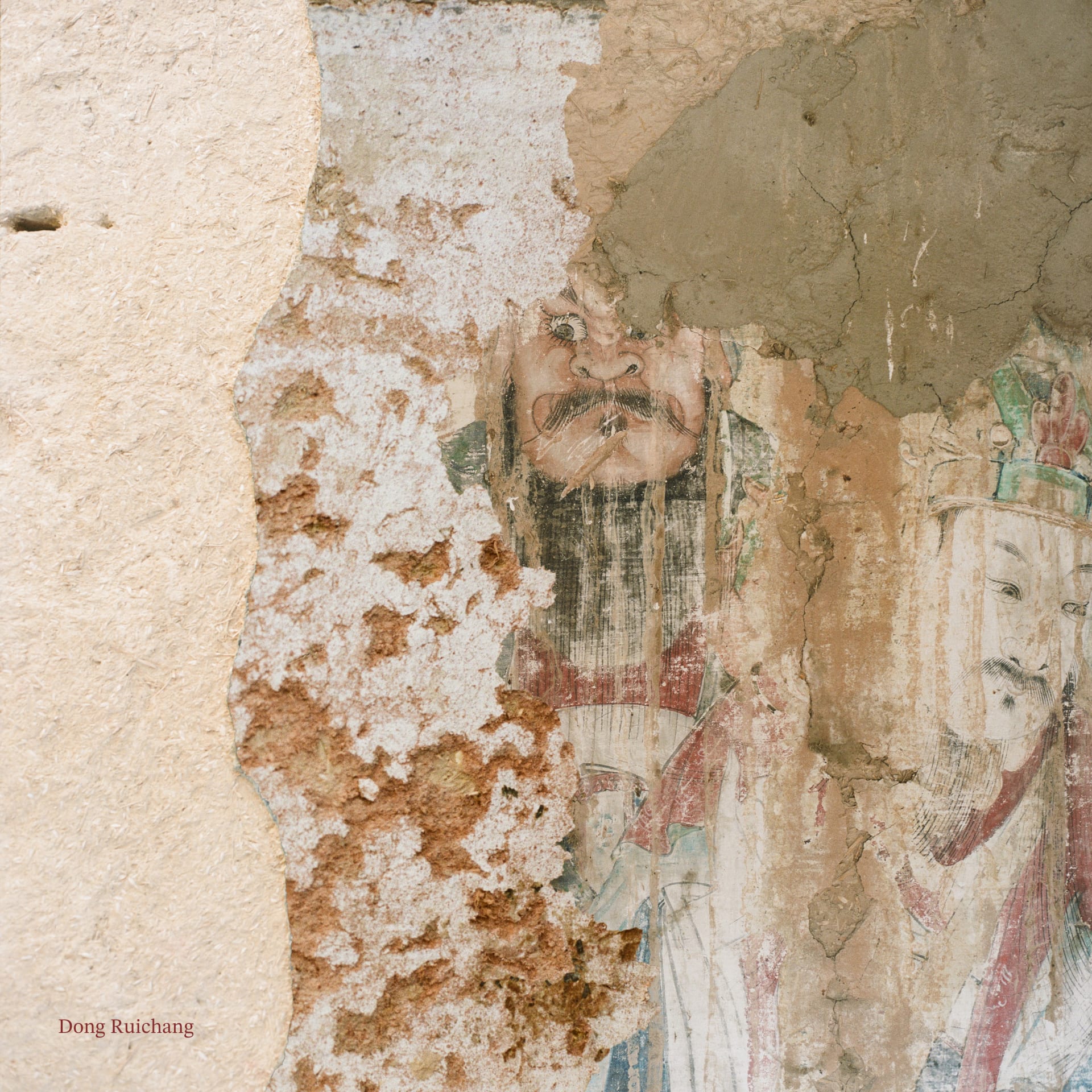 A faded mural of two figures partly visible on a crumbling clay wall.