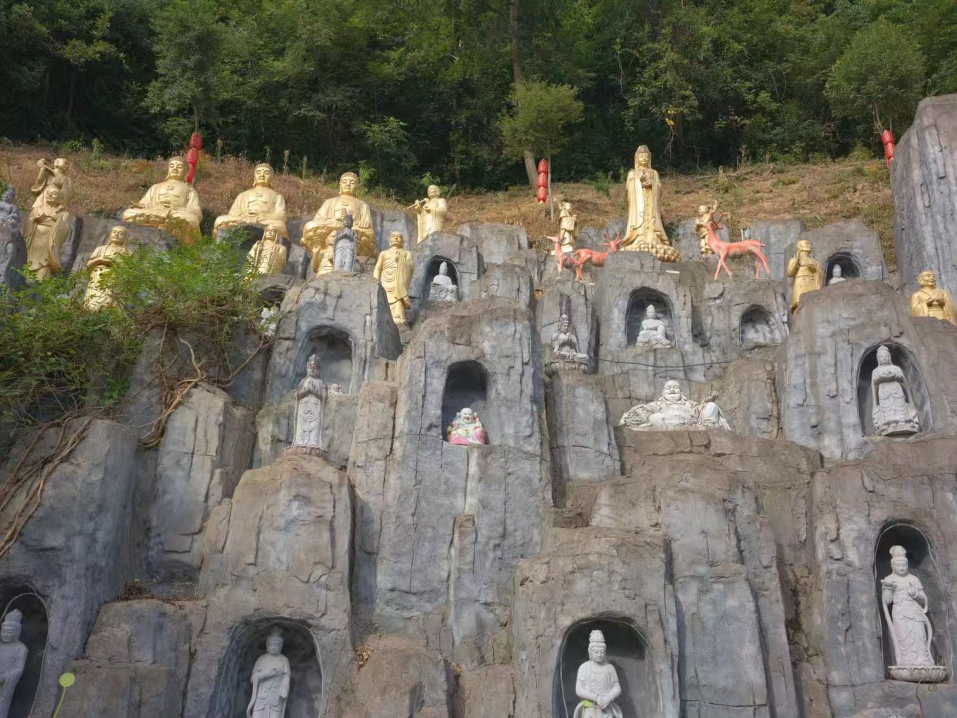 Among the man-made rock formations, Buddha statues of various sizes stand placed so that one must look up to see them, with forests stretching behind