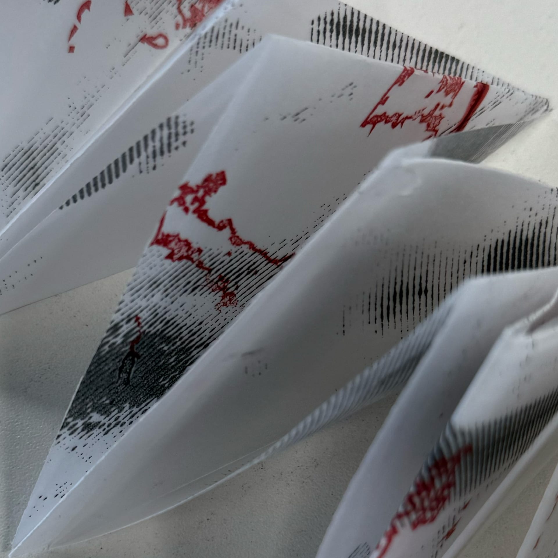 Translucent paper with grey and red screen-printing. Paper has been folded into a triangular accordion.