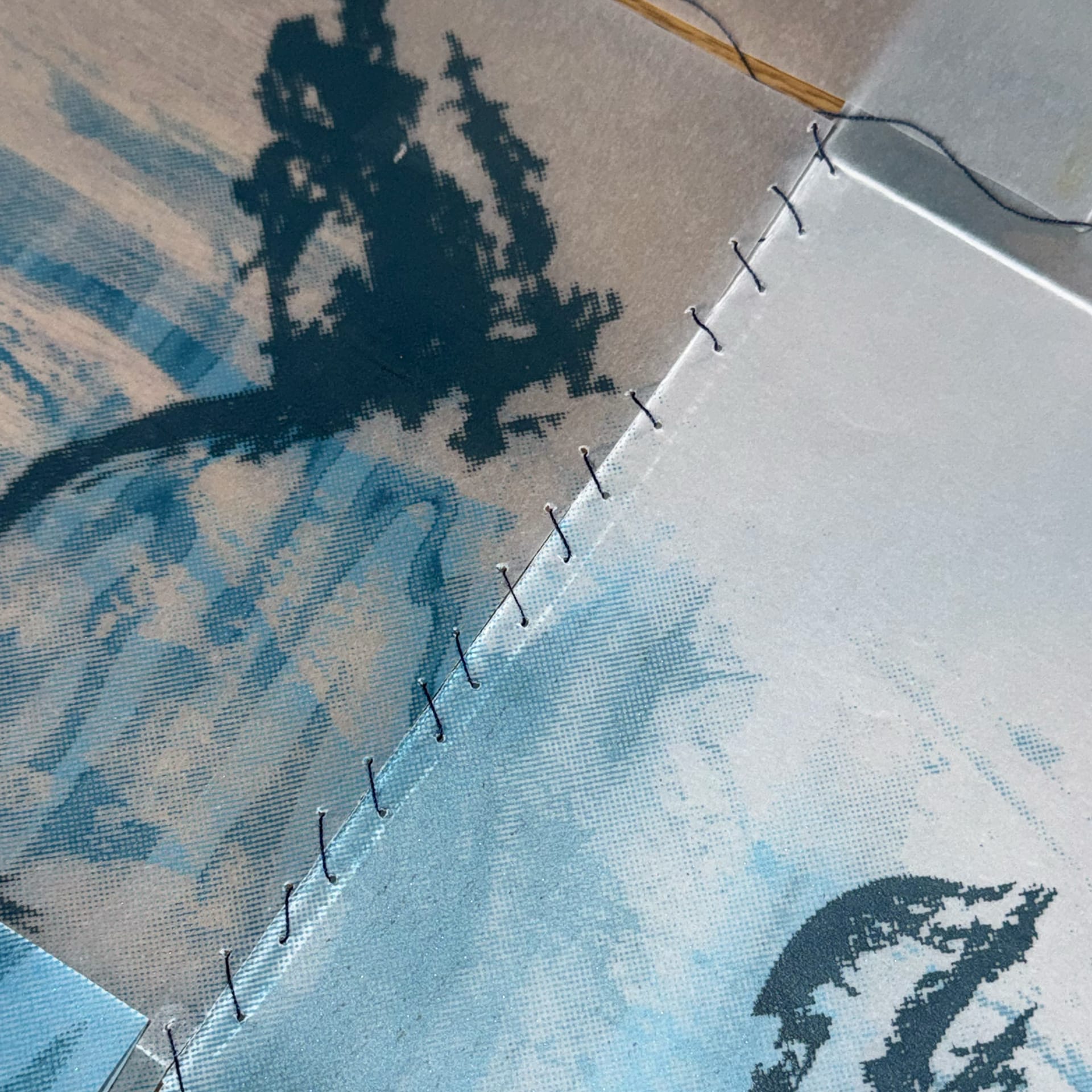 Two pieces of translucent paper imperfectly stitched together in blue thread. Paper has been screen-printed on in blue ink.