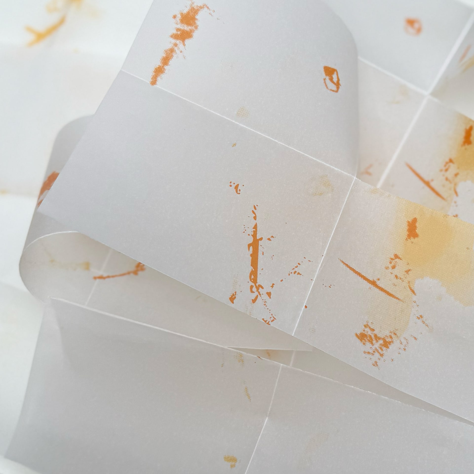 Unfolded concertina of translucent paper that has been screen-printed on in yellow and orange ink.