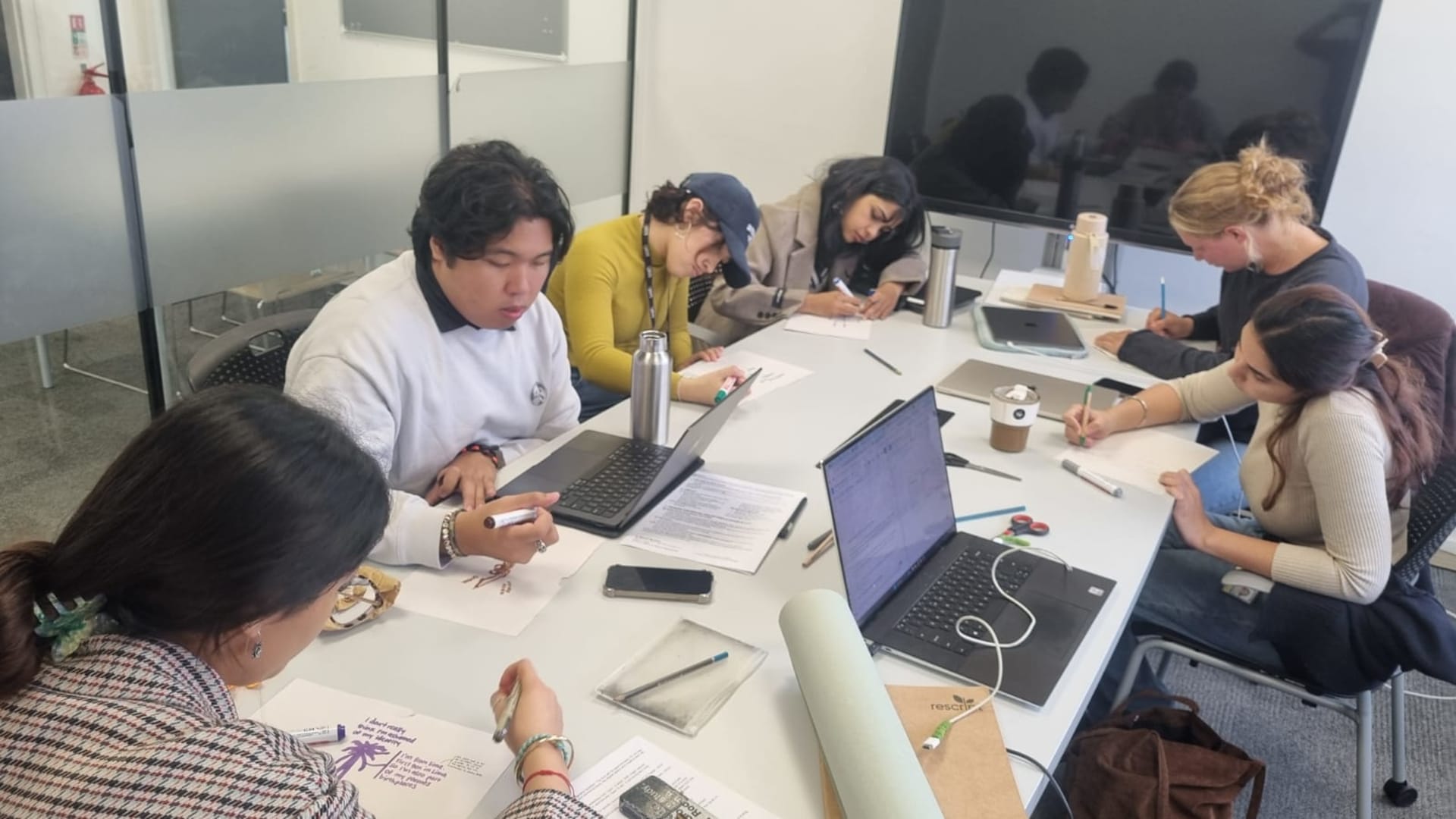 A photograph shows several people seated around a table, actively engaged in a hands-on workshop. Participants are drawing and writing.
