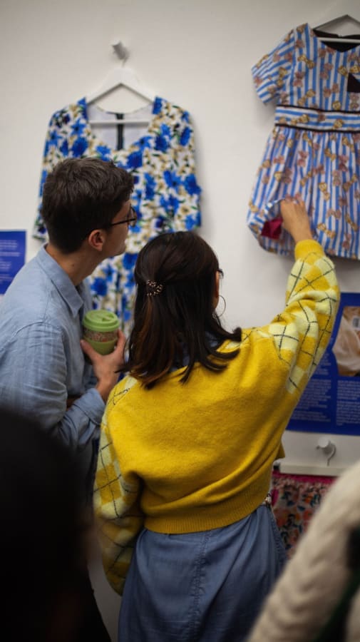2 people looking at and touching garments hanging on wall