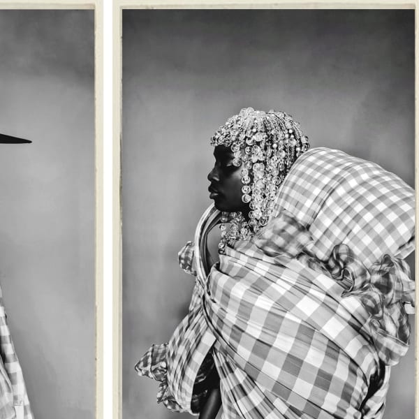 A person wearing a hat facing another person. Both are wearing garments made from a checked material. 