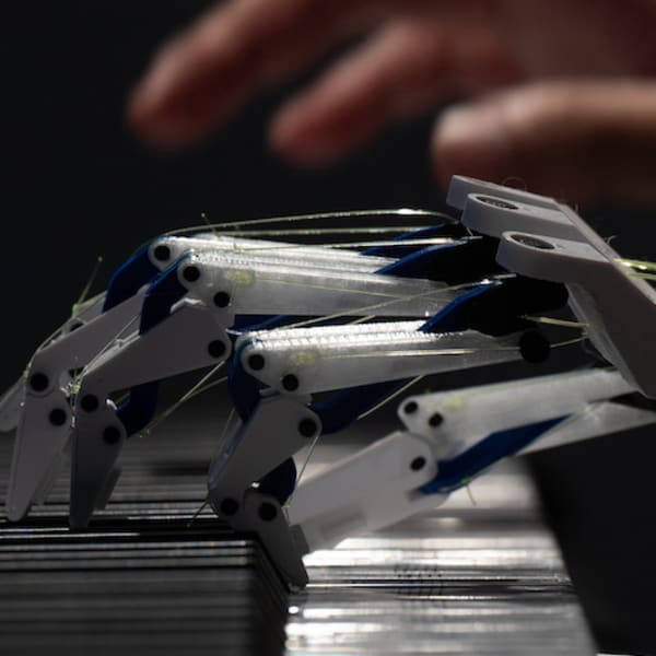 a human hand and a robot hand playing a keyboard