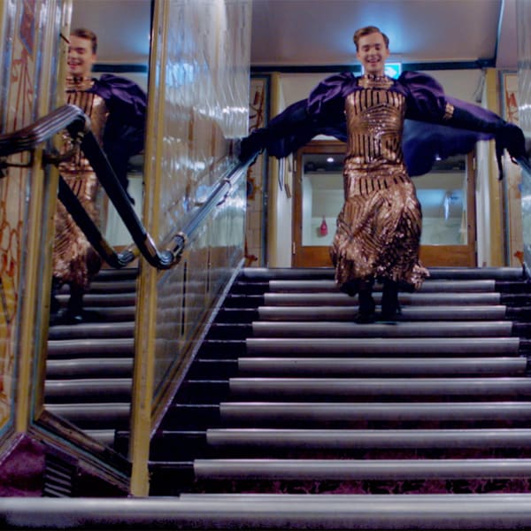 A figure leaps down a staircase within a lavish interior.
