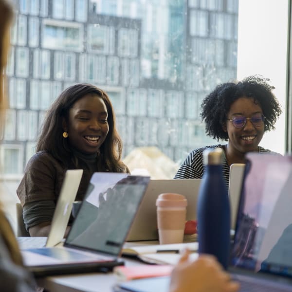Two young women laughing and looking at their laptops