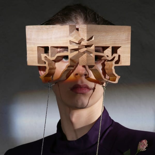 Butterfly-shaped wooden eyewear modeled by male in purple suit.