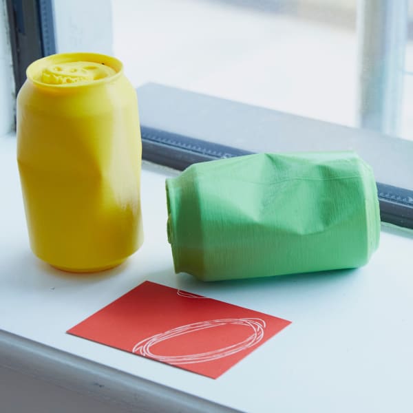 Yellow and green moulded sculptures of drinks cans alongside a red card with white drawn lines. Installation by Carmen Van Huisstede - MA Fine Art: Sculpture, Camberwell College of Arts.