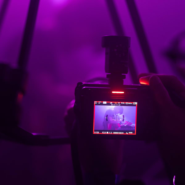 A camera viewfinder shooting a live act on stage, purple stage lighting fills the shot