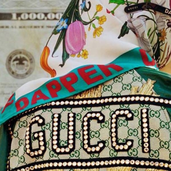 Female model wearing Dapper Dan sunglasses and scarf with paper bill in the background. 